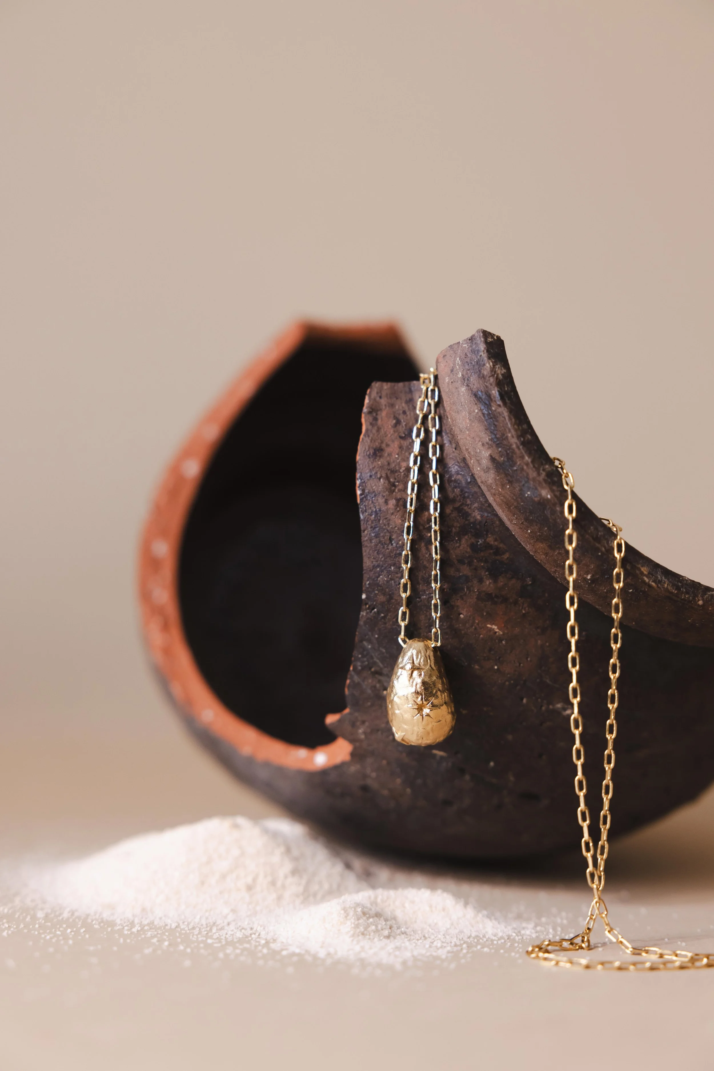 Nature morte d'un collier en or en studio posé sur un pot cassé