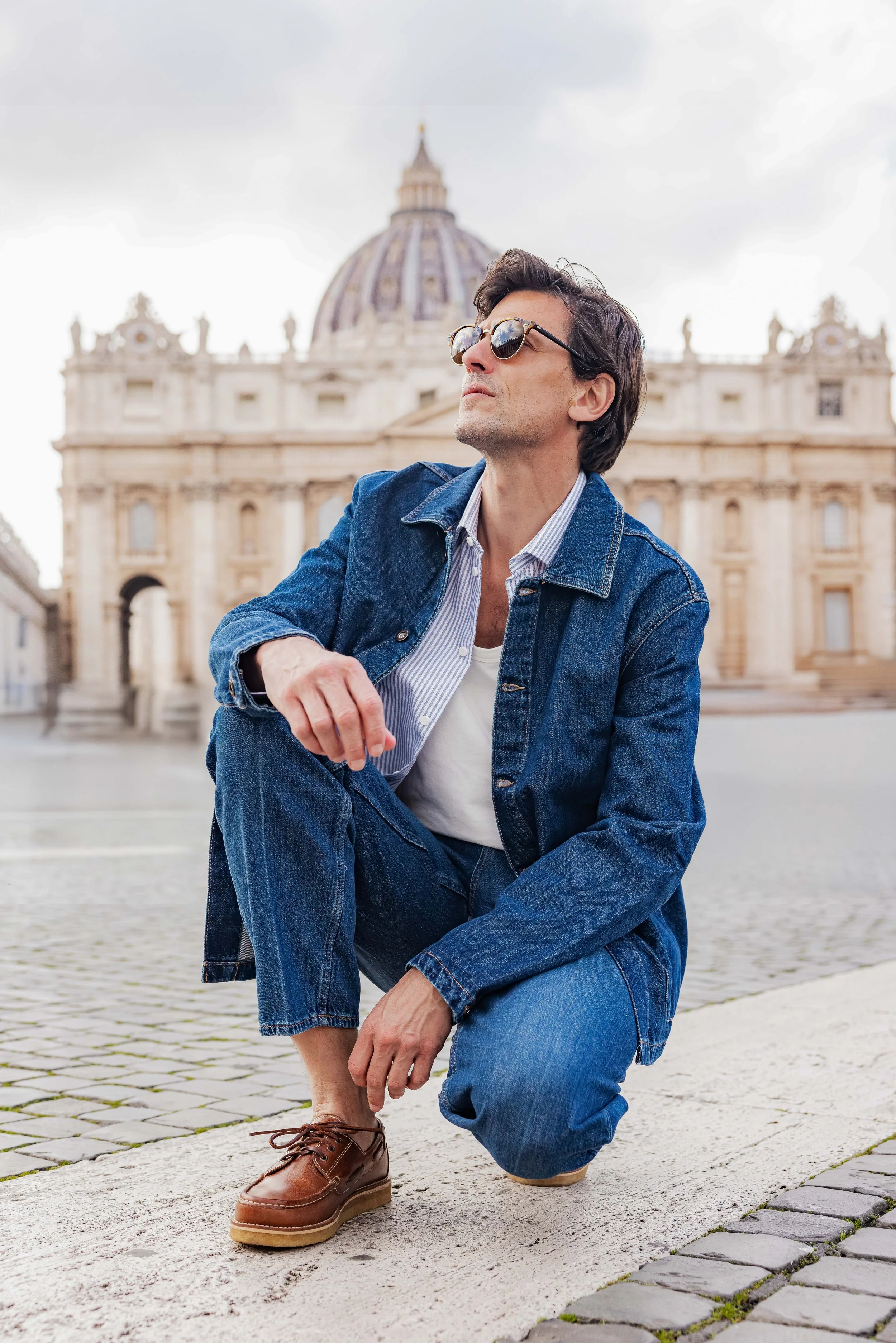Mannequin homme portant une tenue toute en jean et posant accroupi devant le vatican
