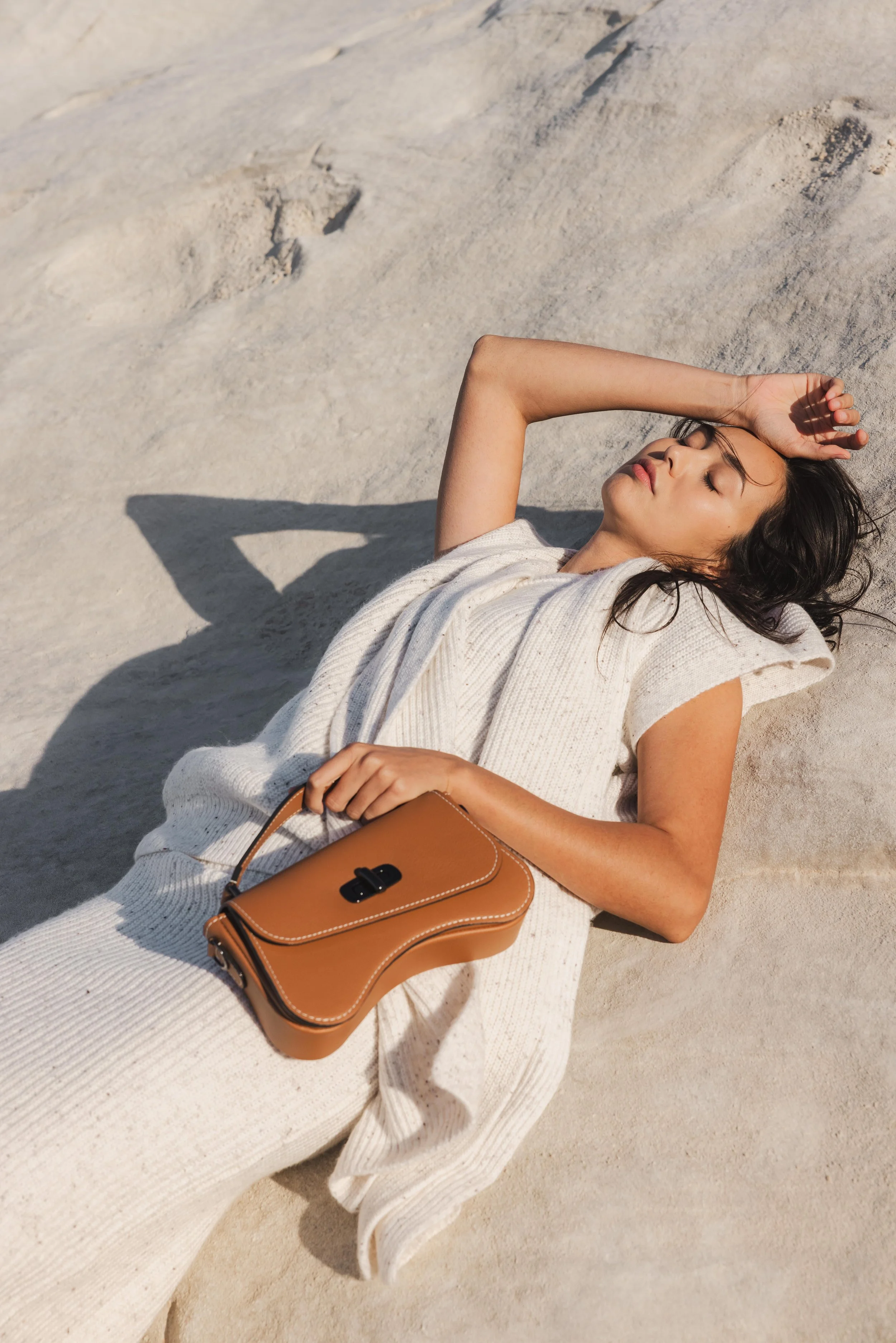Mannequin allongée portant un sac en cuir marron sur une surface minérale en lumière naturelle