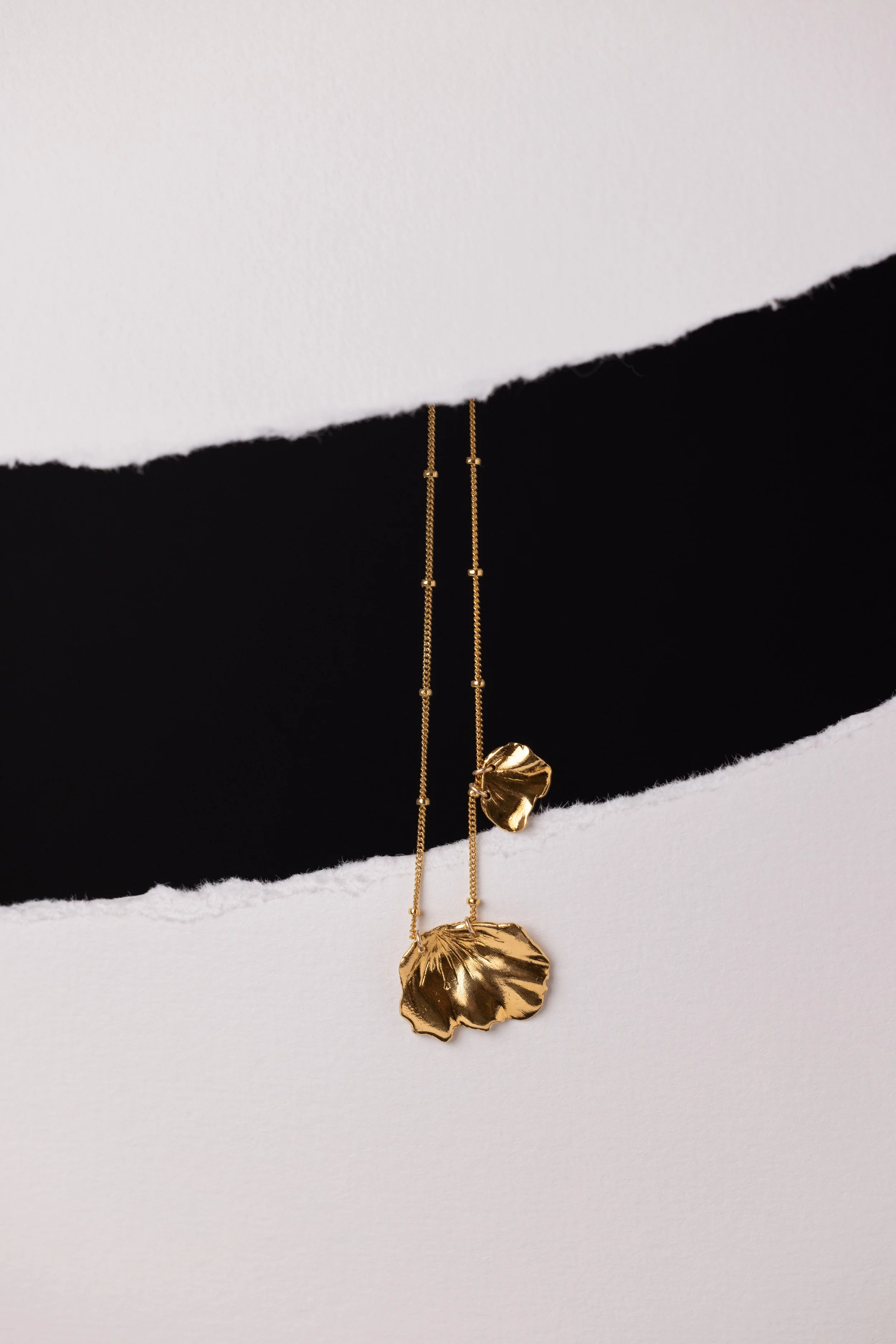 Collier en or suspendu entre deux pans d'une feuille déchirée