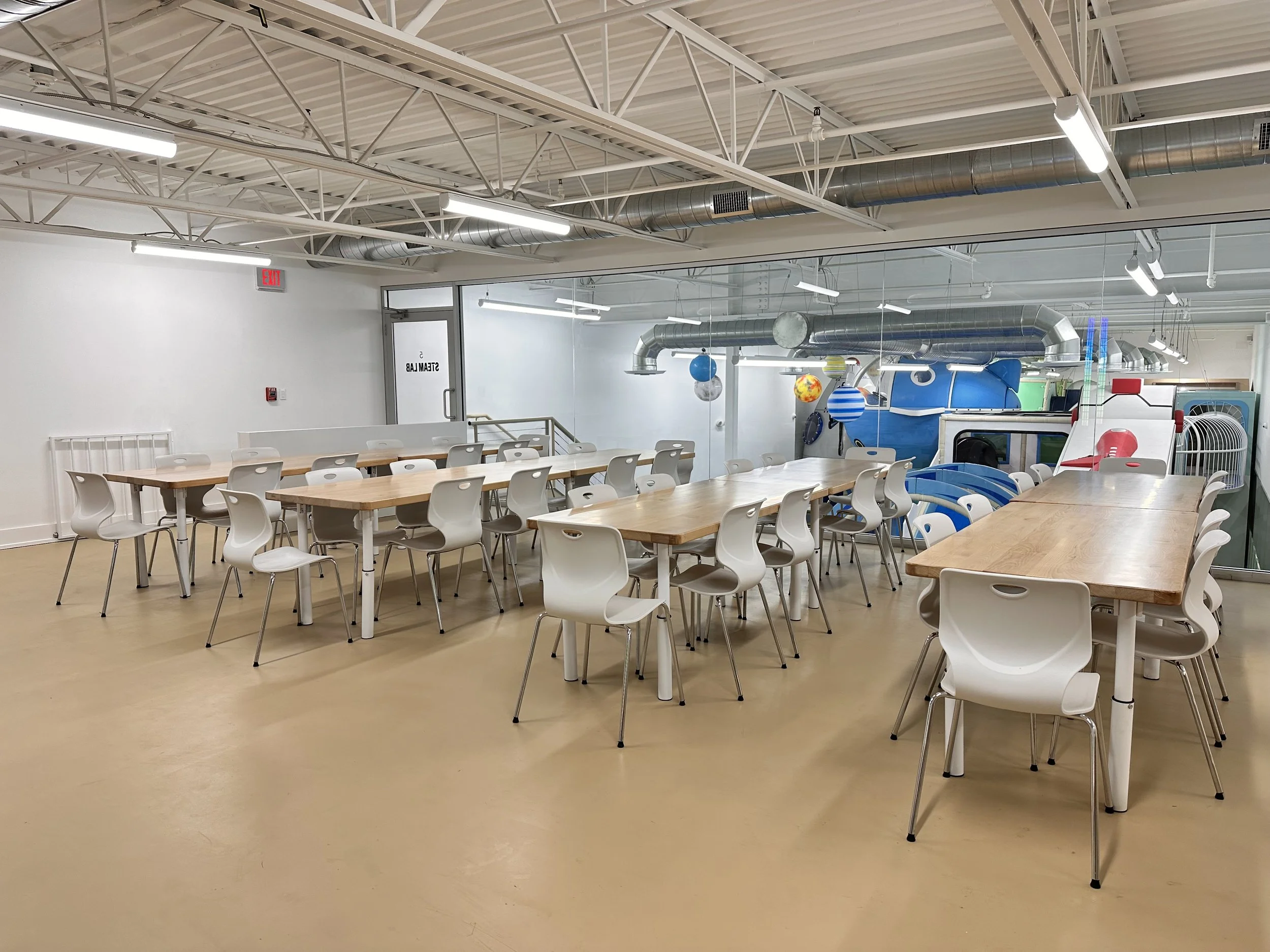 Our STEAM Lab with wood tables and a view of the play space.
