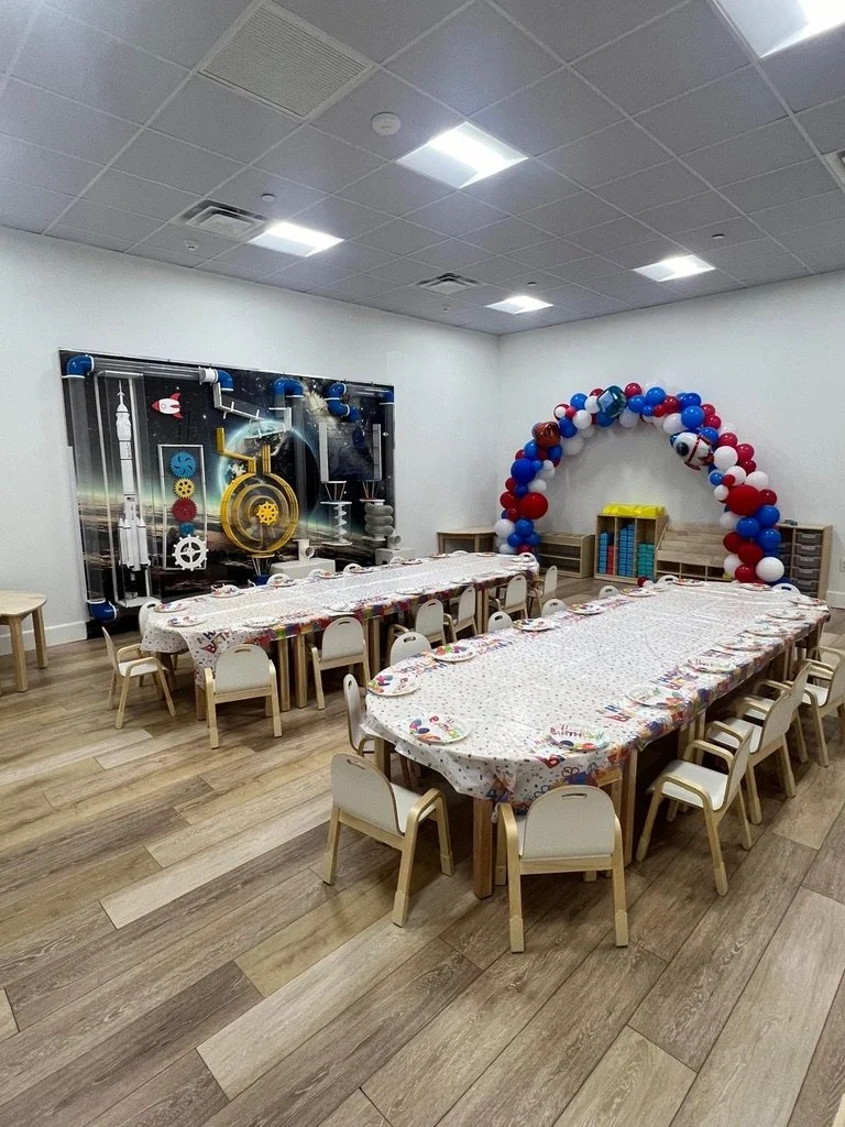 Our Junior Navigators Room with an interactive wall, wood floors and children's tables and chairs.