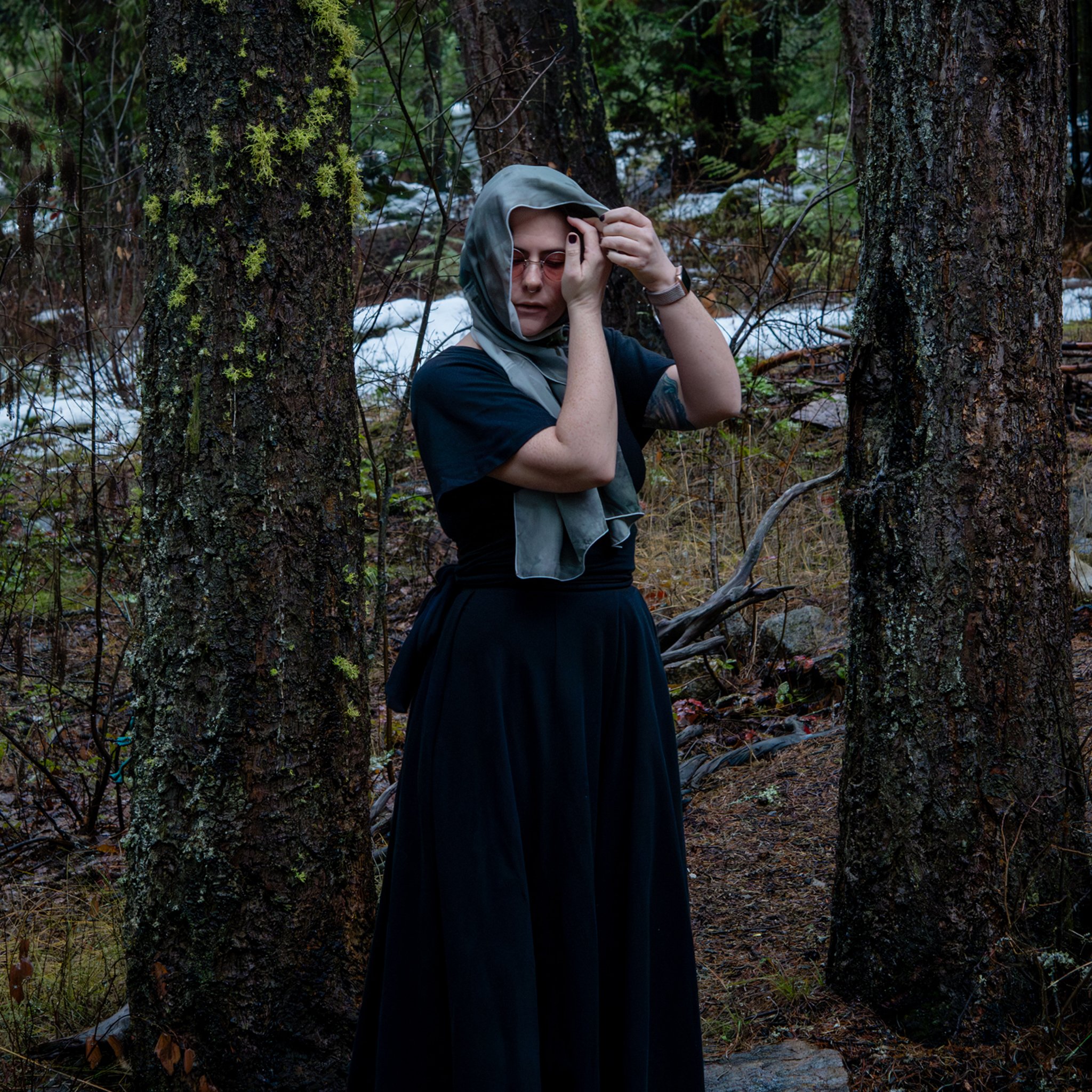 Tua from Coven Mail wearing a black dress with a silvery grey veil stood in the forest