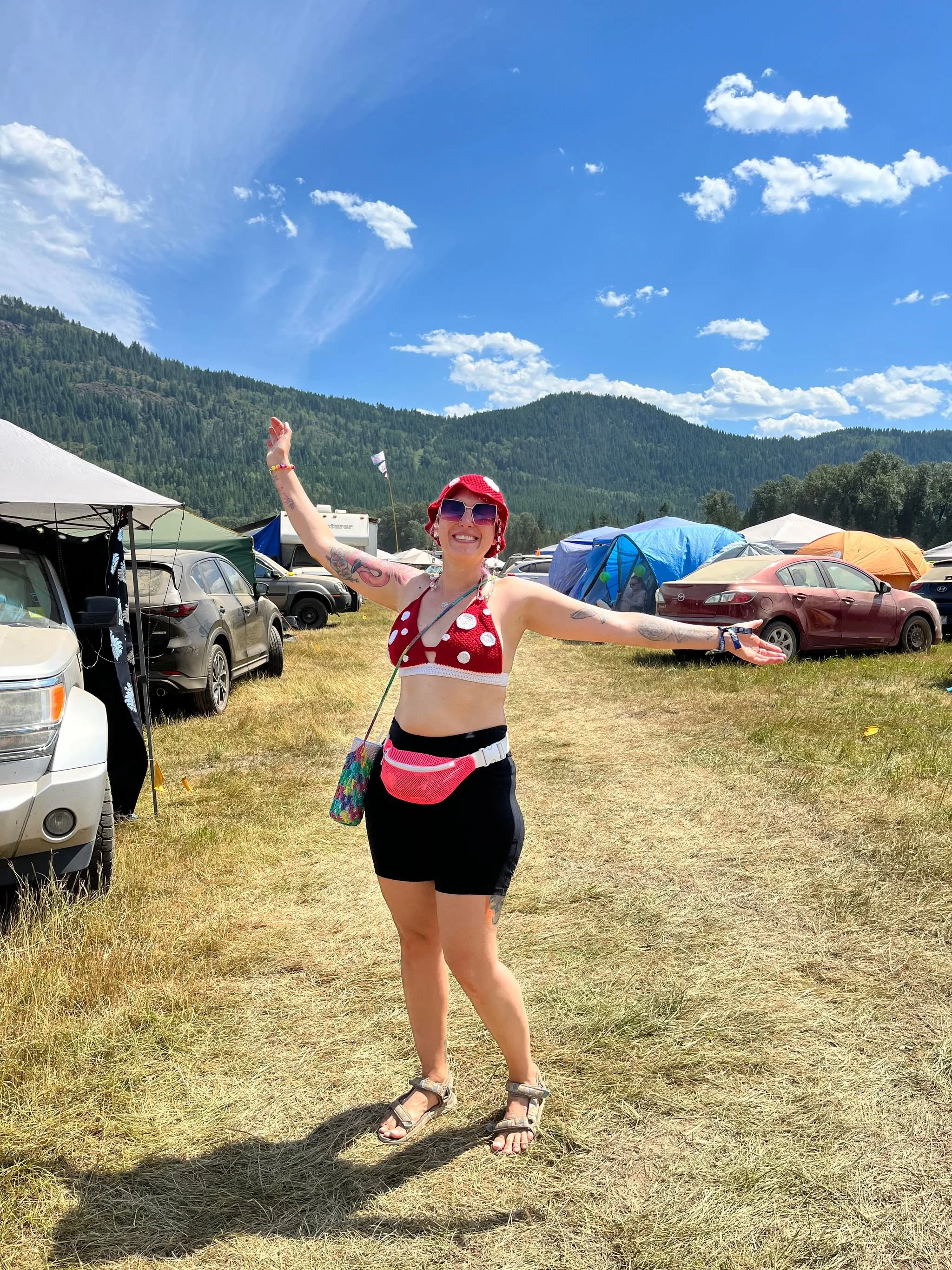 Woman smiling with arms outstretched at Shambhala Music Festival in Salmo, BC. She is wearing a crochet bralette and bucket hat, custom made by Butterflies in Ballgowns in Nelson BC