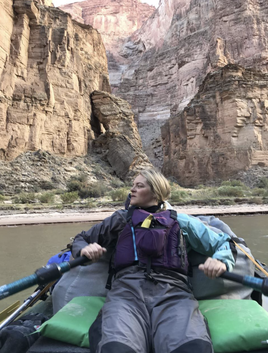 Woman kayaking on a river surrounded by steep canyon cliffs.