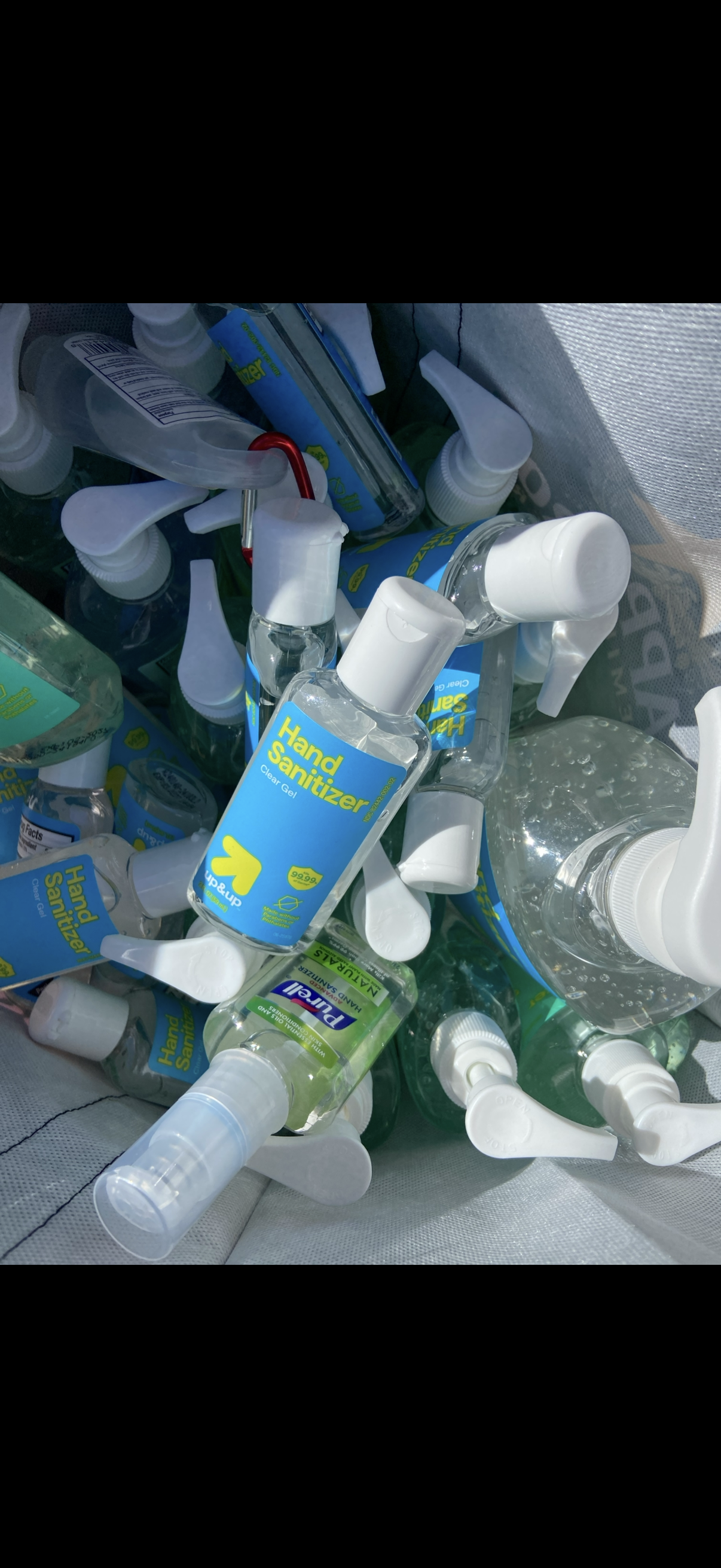 Collection of disinfectant hand sanitizers with spray nozzles and labels, some bottles upright and others tilted, in a fabric container.