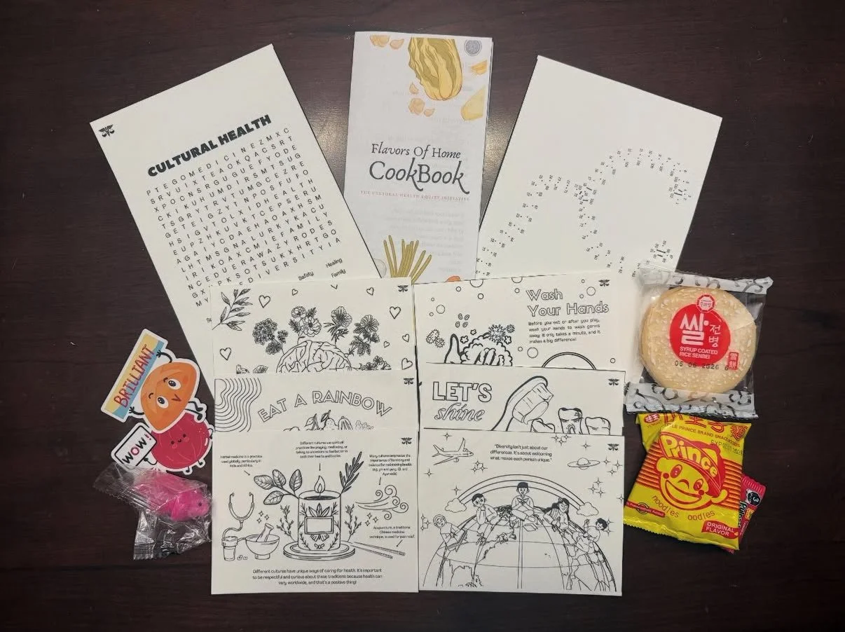 Collection of printed sheets with illustrations and text, snacks including rice crackers, a cookie, and a candy, along with a cardboard sticker of a cartoon orange character.