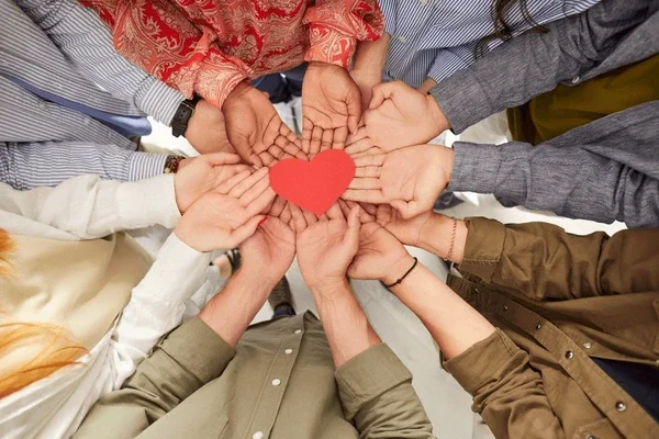 Multiple hands forming a heart shape around a red paper heart.