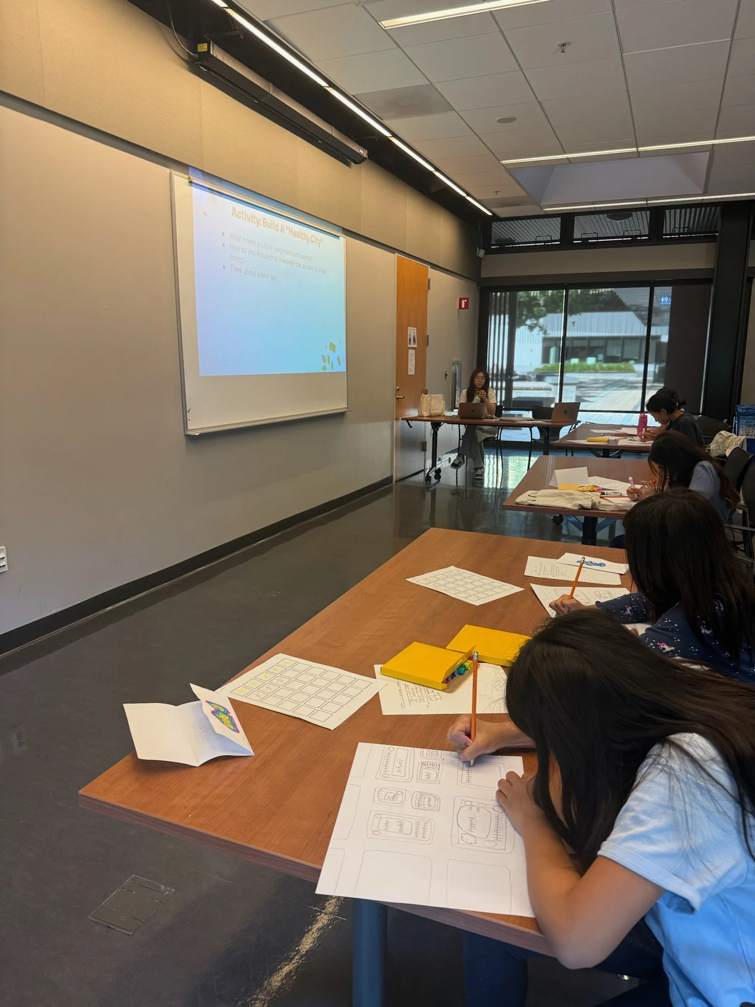 People participating in a workshop or class in a conference room, taking notes and engaging with presentation slides projected on a wall.