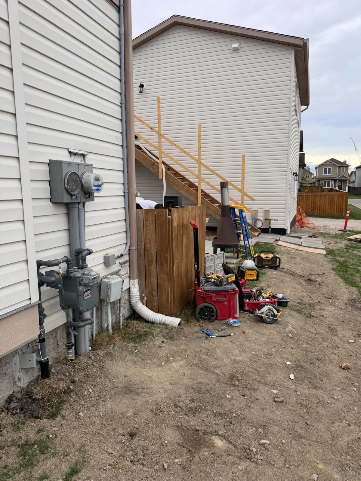 Two electrical meters on the side of a house in Okotoks during construction, with the exterior stairs to the suite above the garage behind