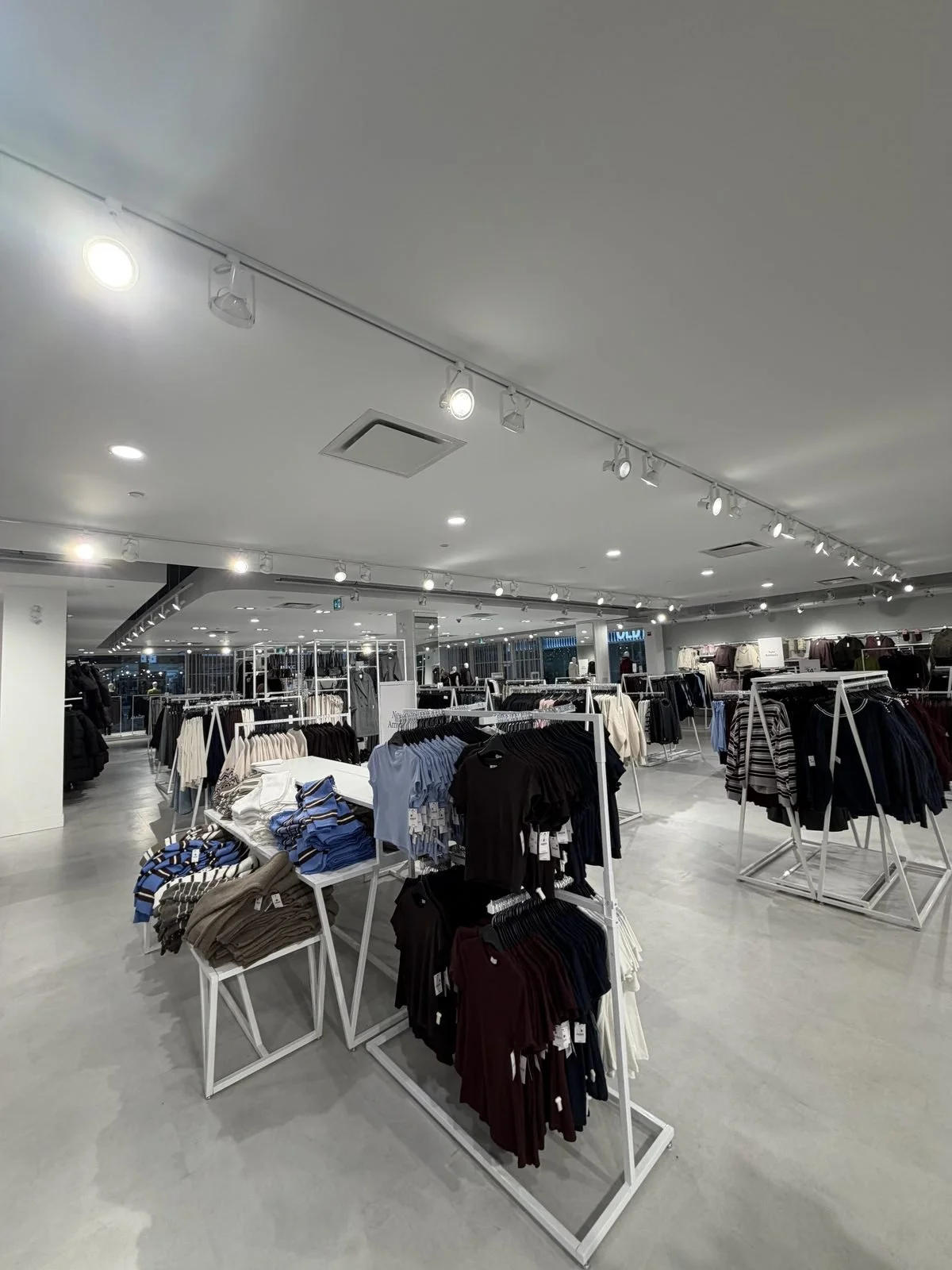 Row of white track lighting heads on the ceiling of the Ardene sales floor, some lit and some out, before the retrofit