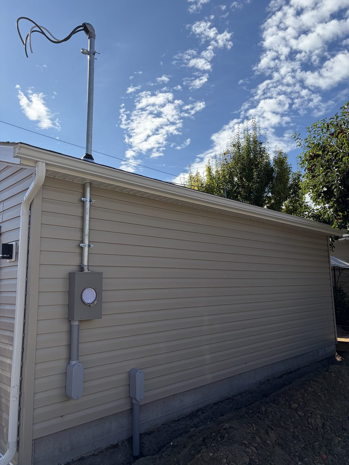 New 200 amp service mast and meter base installed by Koop Electrical on the alley side of a detached garage in Dover, Calgary, with the overhead drop ending at the garage roof