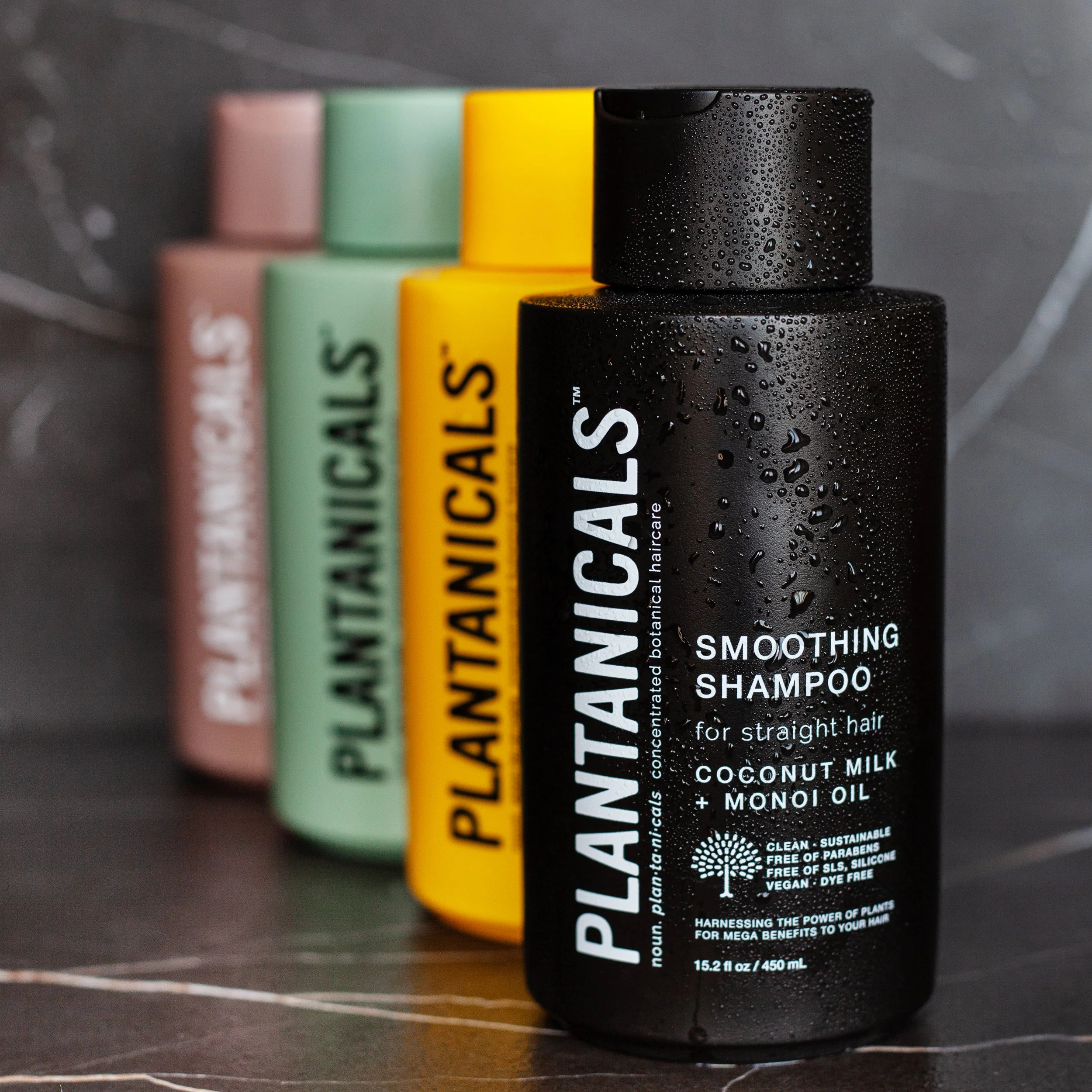 Black bottle of facial hair smoothening shampoo with water droplets on it, featuring white text, alongside pastel-colored bottles in pink, green, and yellow, on a dark background.