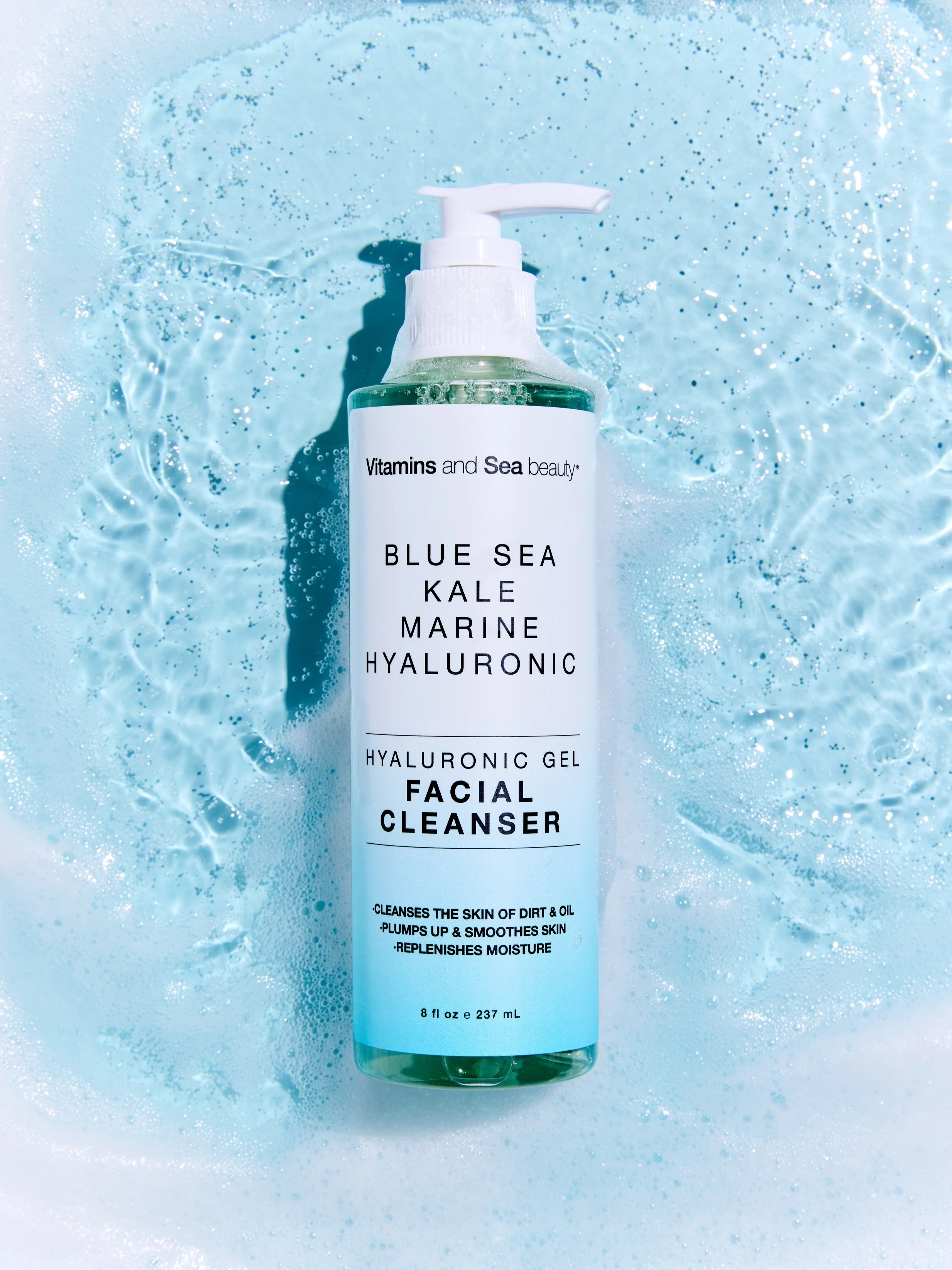 A clear bottle of facial cleanser labeled 'Vitamins and Sea Beauty Blue Sea Kale Marine Hyaluronic' with a white pump dispenser, set against a background of icy blue water and bubbles.