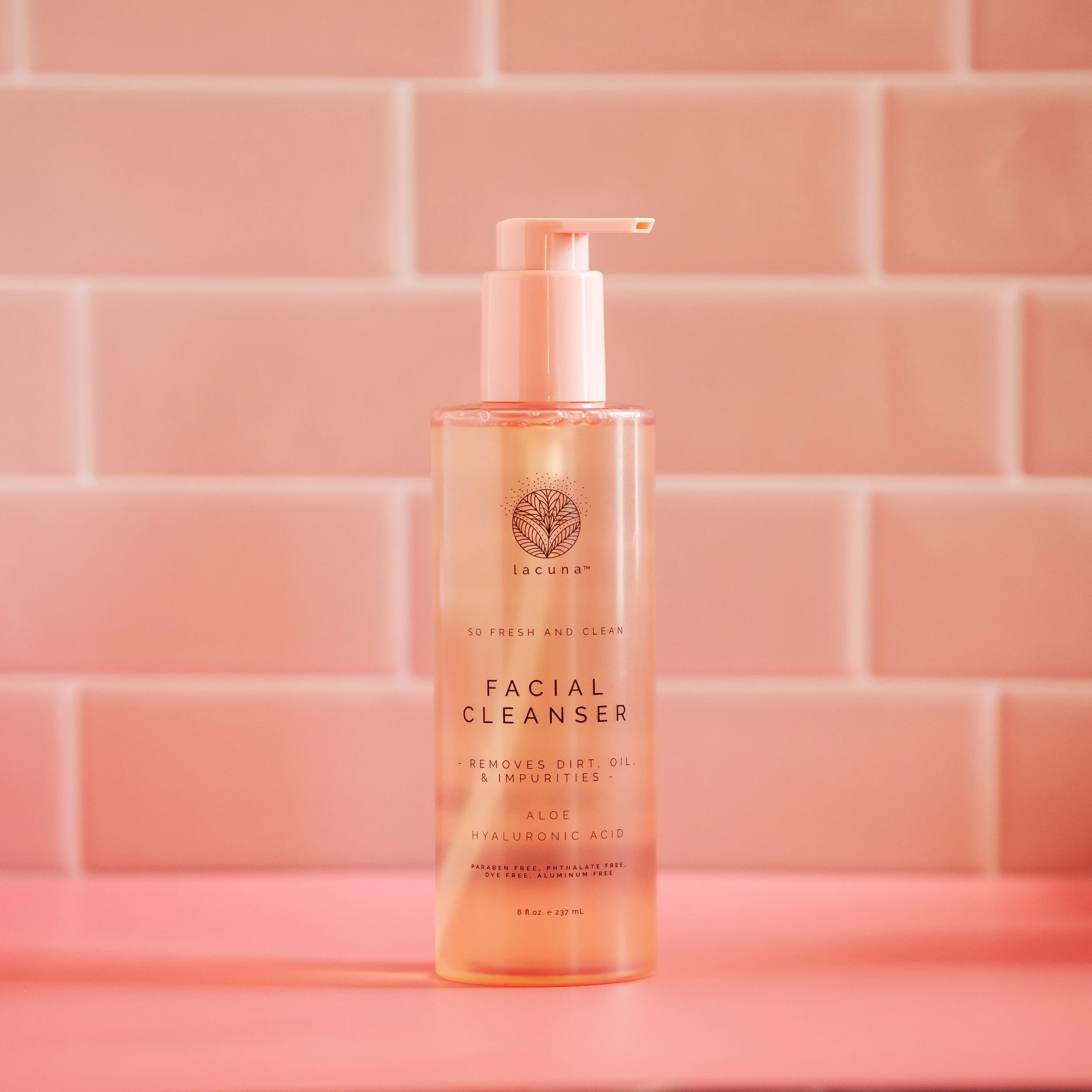 A bottle of facial cleanser with a pump dispenser against pink tiled background.