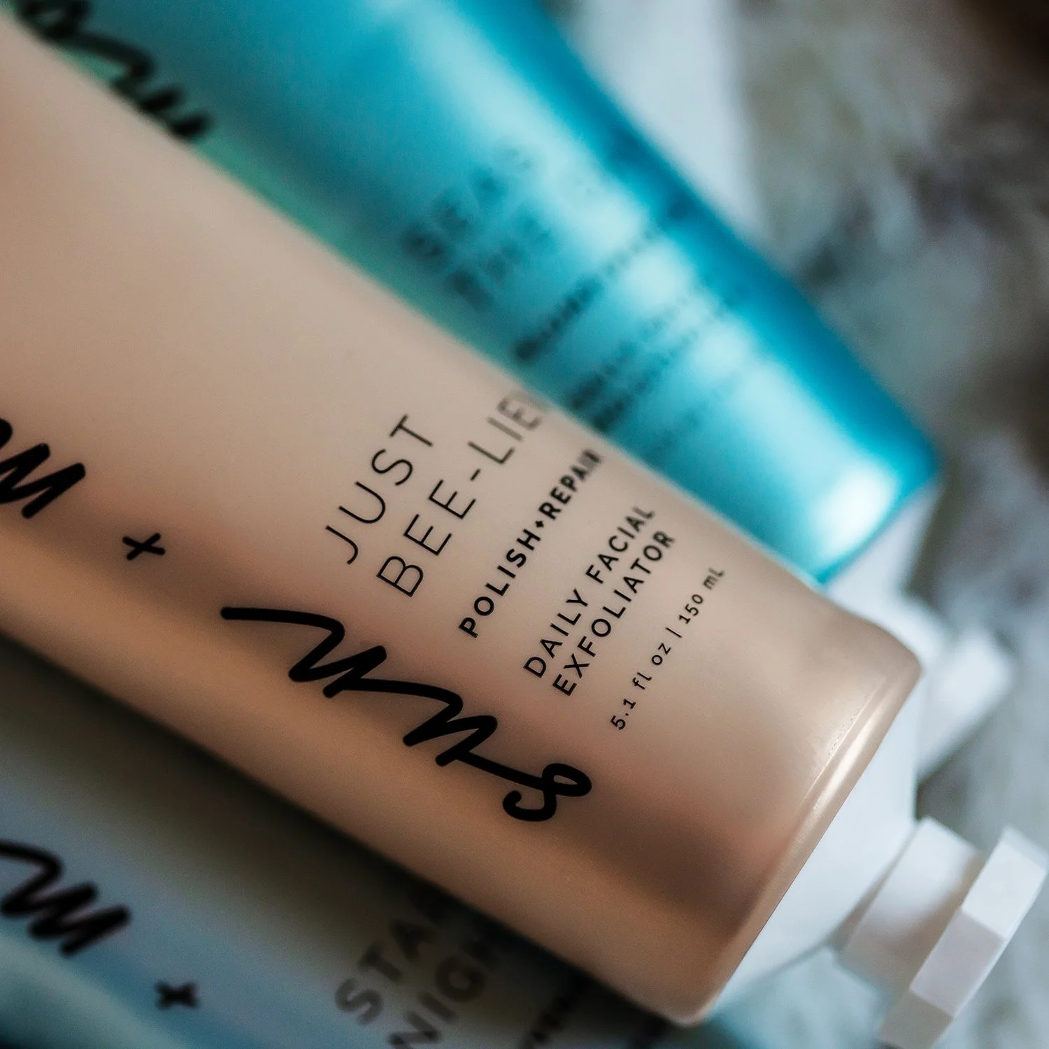 Close-up of a tube of skincare product, Likely a facial exfoliator, with text indicating it is a 'Just Be-Lieve Daily Facial Exfoliator' in a 5.1 fl oz (150 ml) size.