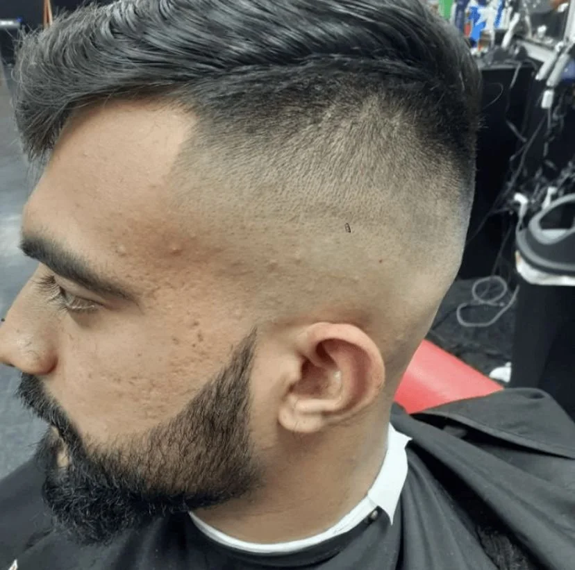 Side profile of a men's comb-over fade with a sharp line-up and trimmed beard, cut by Ben Santiago at Gem City Barbers in Erie, PA.