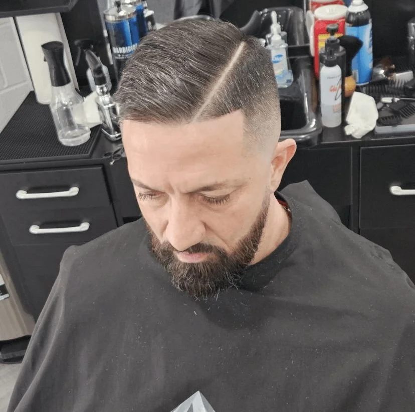 Top-down view of a men's hard part comb-over with a mid skin fade and full beard, cut by Ben Santiago at Gem City Barbers in Erie, PA.