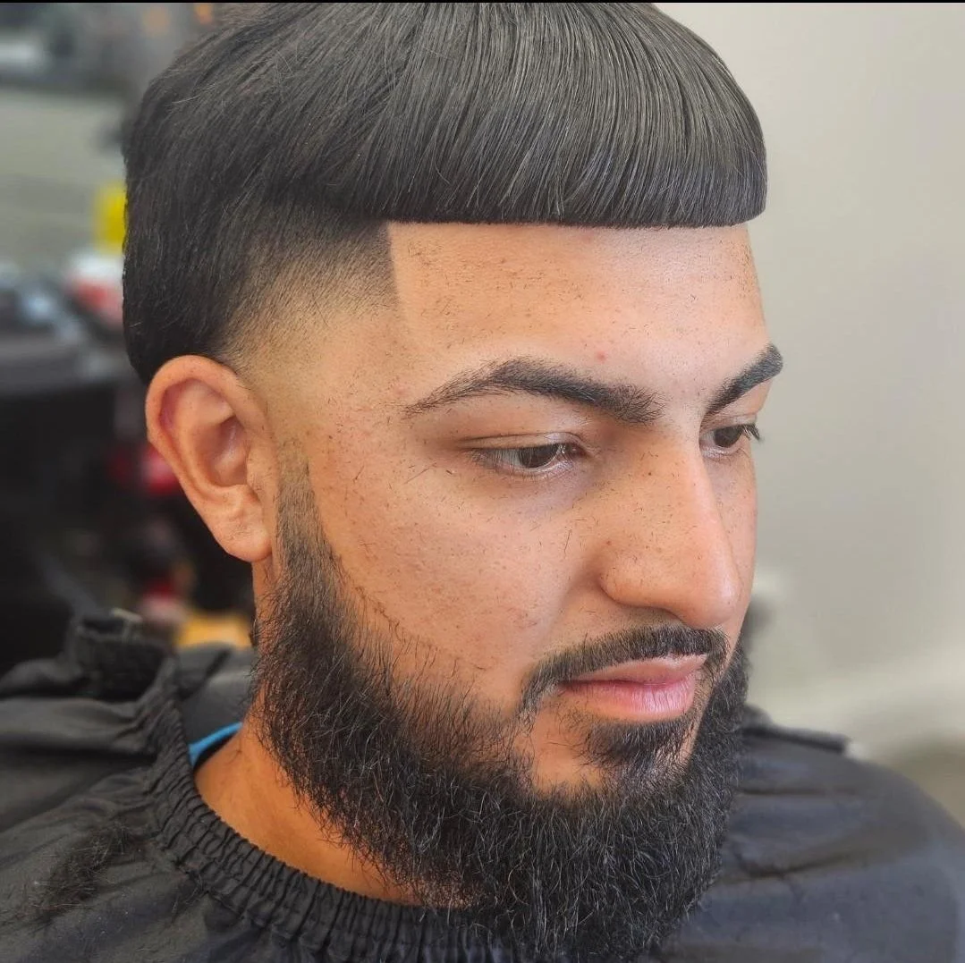 Front view of a men's bowl cut with a blunt fringe line and mid skin fade, paired with a full beard, styled at Gem City Barbers in Erie, PA.