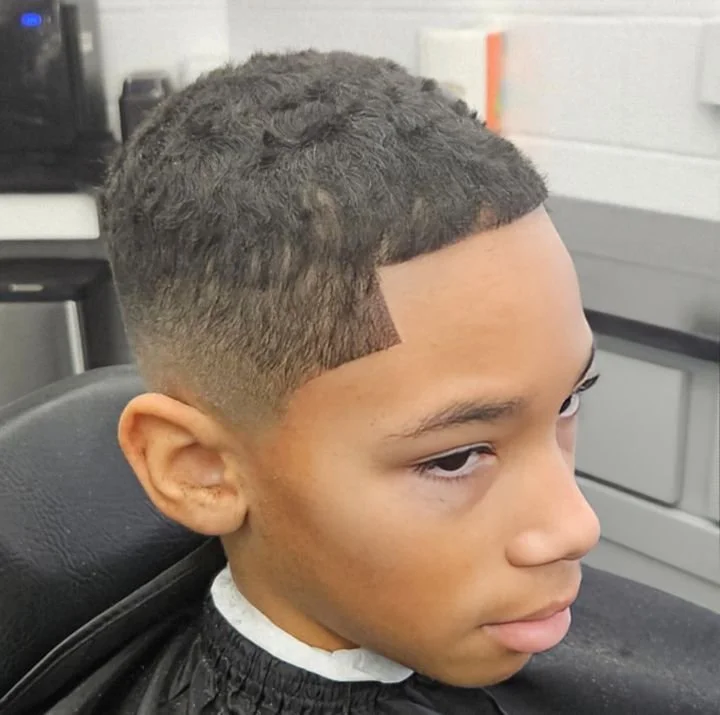 Front and side view of a kid's short curly top haircut with a sharp line-up and low taper fade, cut at Gem City Barbers in Erie, PA.