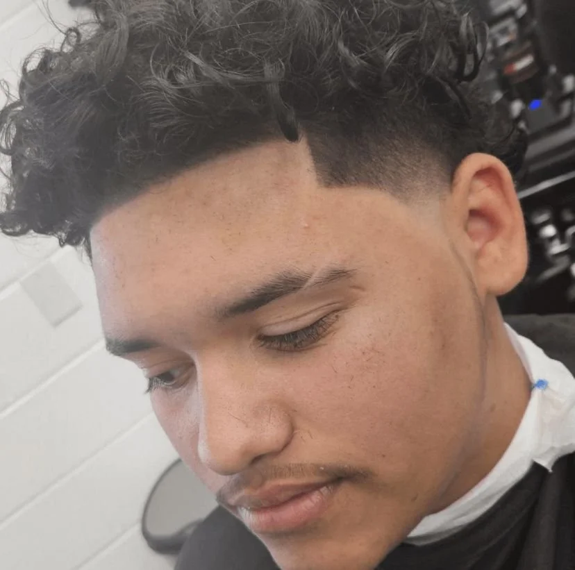 Front view of a men's curly top with a low taper fade and natural curl definition, cut by Ben Santiago at Gem City Barbers in Erie, PA.