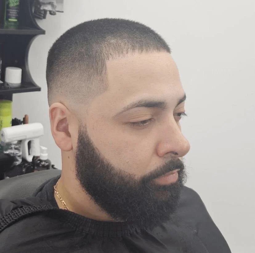 Front and side view of a men's skin fade buzz cut with a full shaped beard, cut by Ben Santiago at Gem City Barbers in Erie, PA.