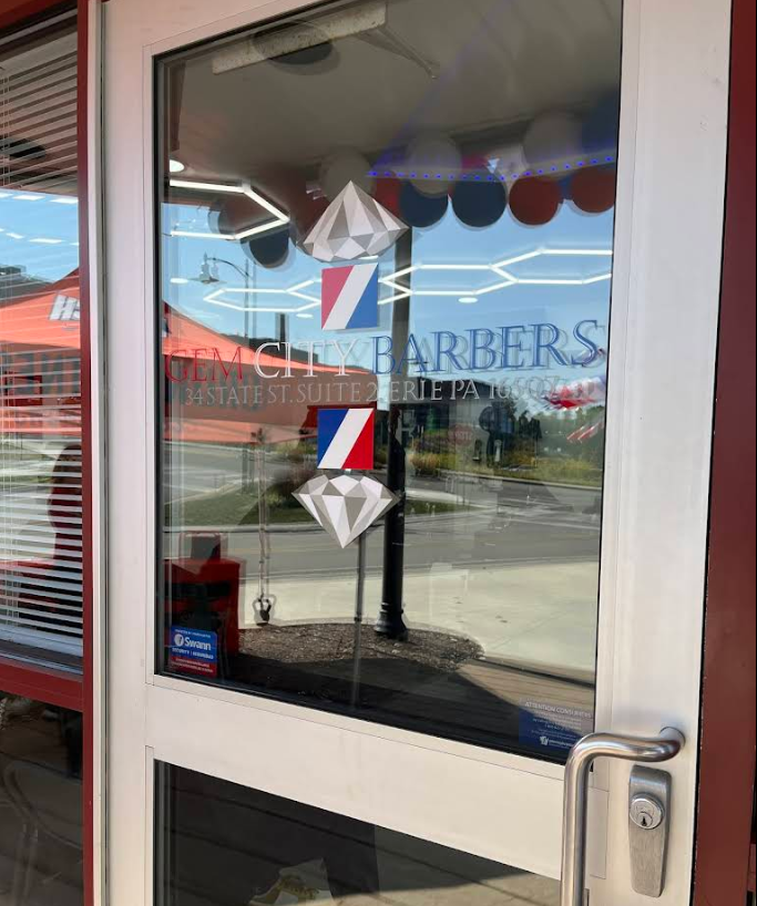 Front door of Gem City Barbers showing the shop's logo with diamond and barber pole graphics, along with the address at 34 State St. Suite 2, Erie, PA.