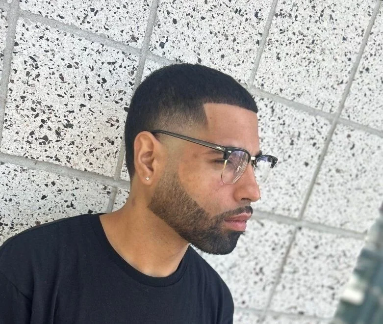 Side profile of a men's low fade with short natural texture on top and a lined beard, cut by Ben Santiago at Gem City Barbers in Erie, PA.