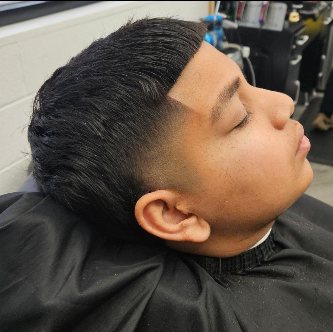 Side view of a young client's slicked-back comb-over haircut with a sharp line-up and taper fade, done at Gem City Barbers in Erie, PA.
