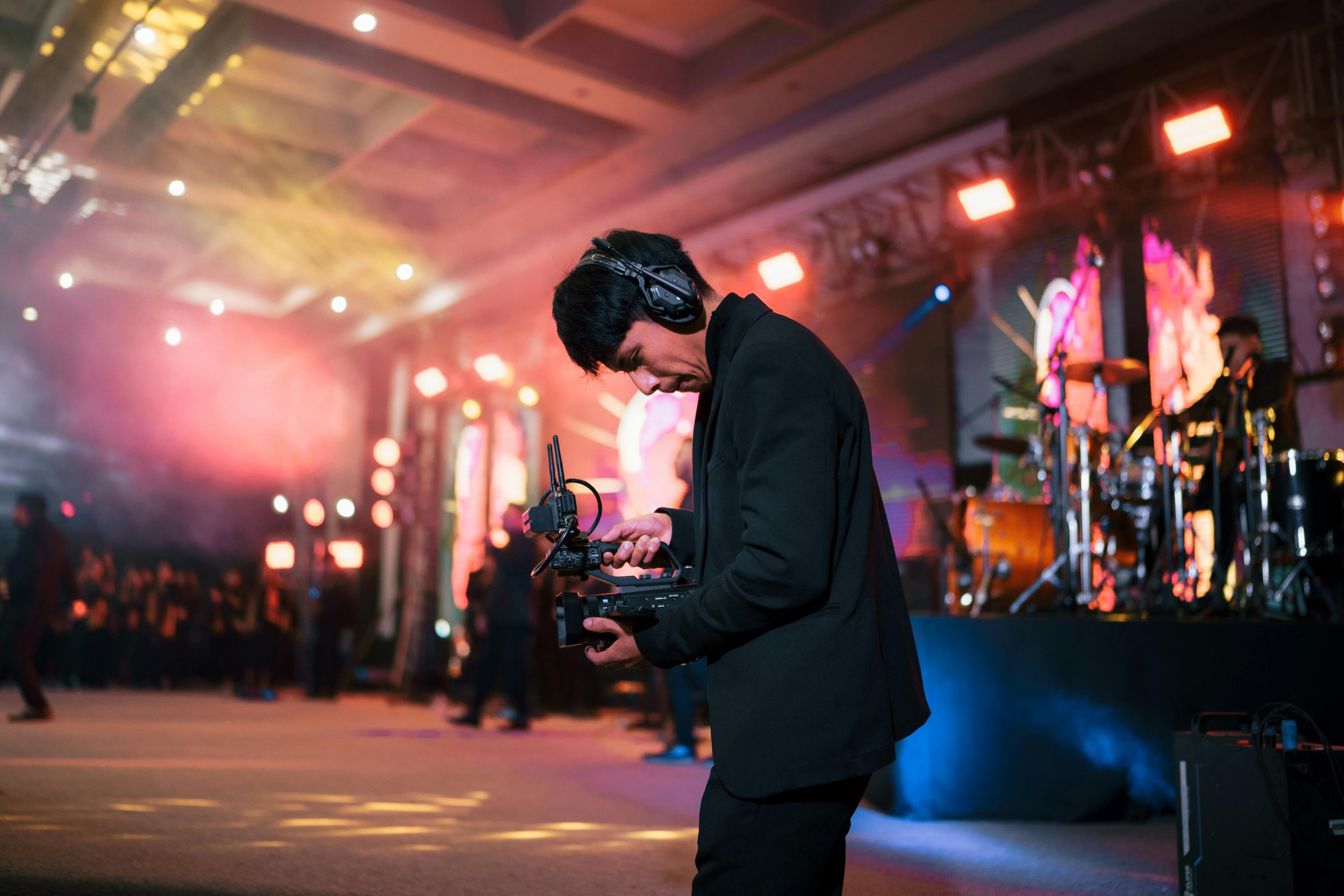 Videographer in Seattle capturing a live event for video production. The scene features colorful stage lighting and a blurry background of other people and stage elements.