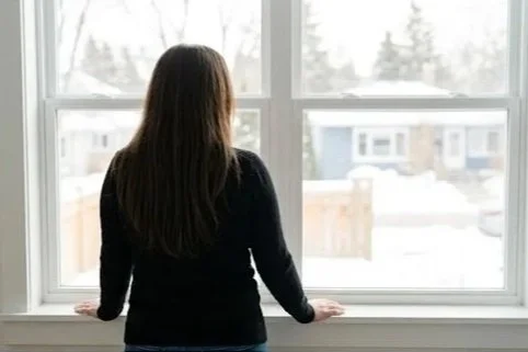 A person with long hair looking out of a large window during daytime.