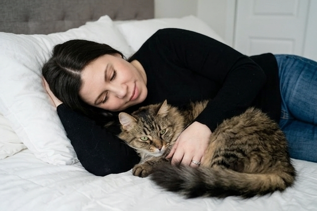 A woman lying on a bed cuddling a large tabby cat.