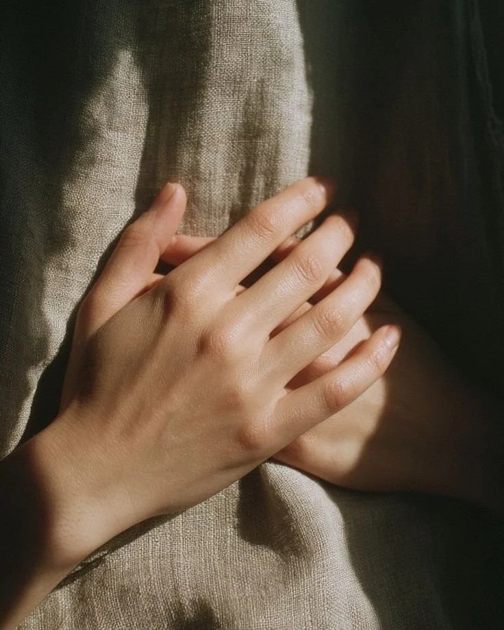 Close-up of a person's hand gently resting on a beige fabric surface with soft lighting.