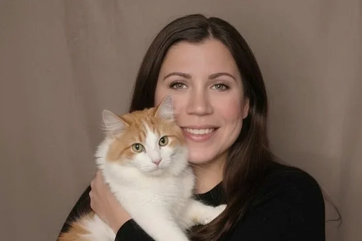 A woman with long dark hair holding a fluffy orange and white cat, both smiling at the camera.