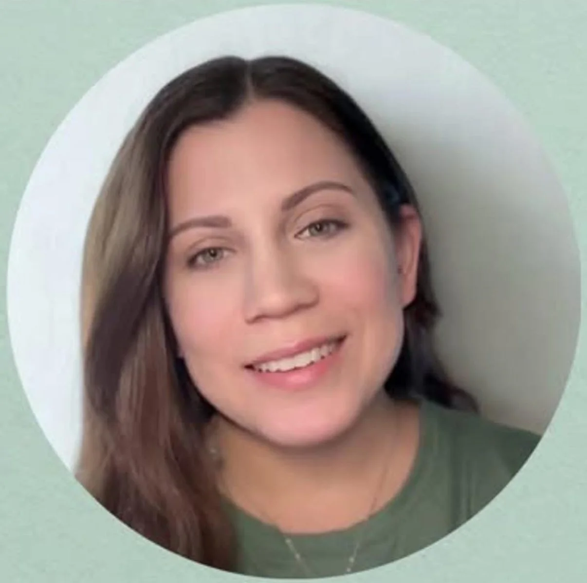 Close-up portrait of a woman with brown hair and light makeup, smiling, wearing a green top, against a light green background.