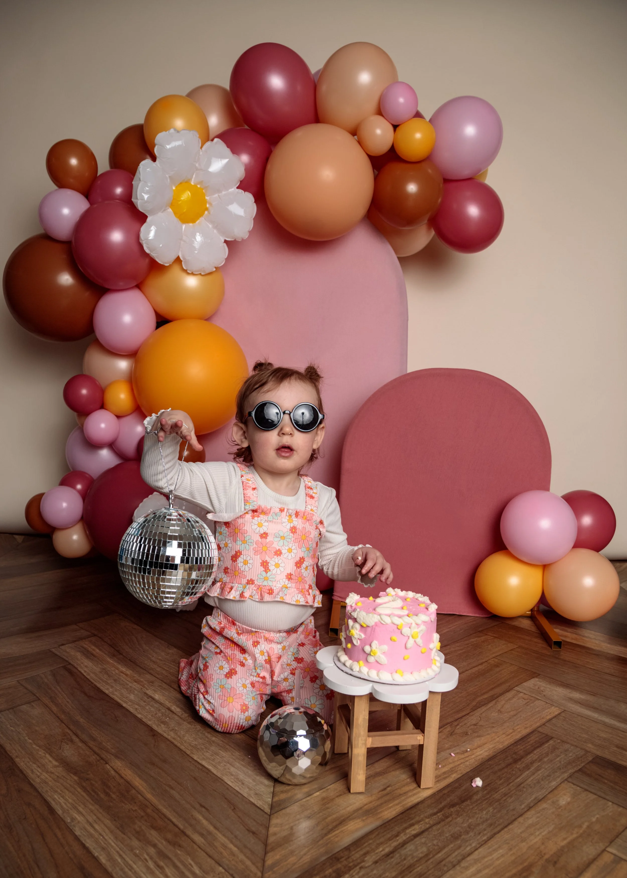 A young girl celebrating her birthday with balloons, a cake, and a disco ball in a decorated room.