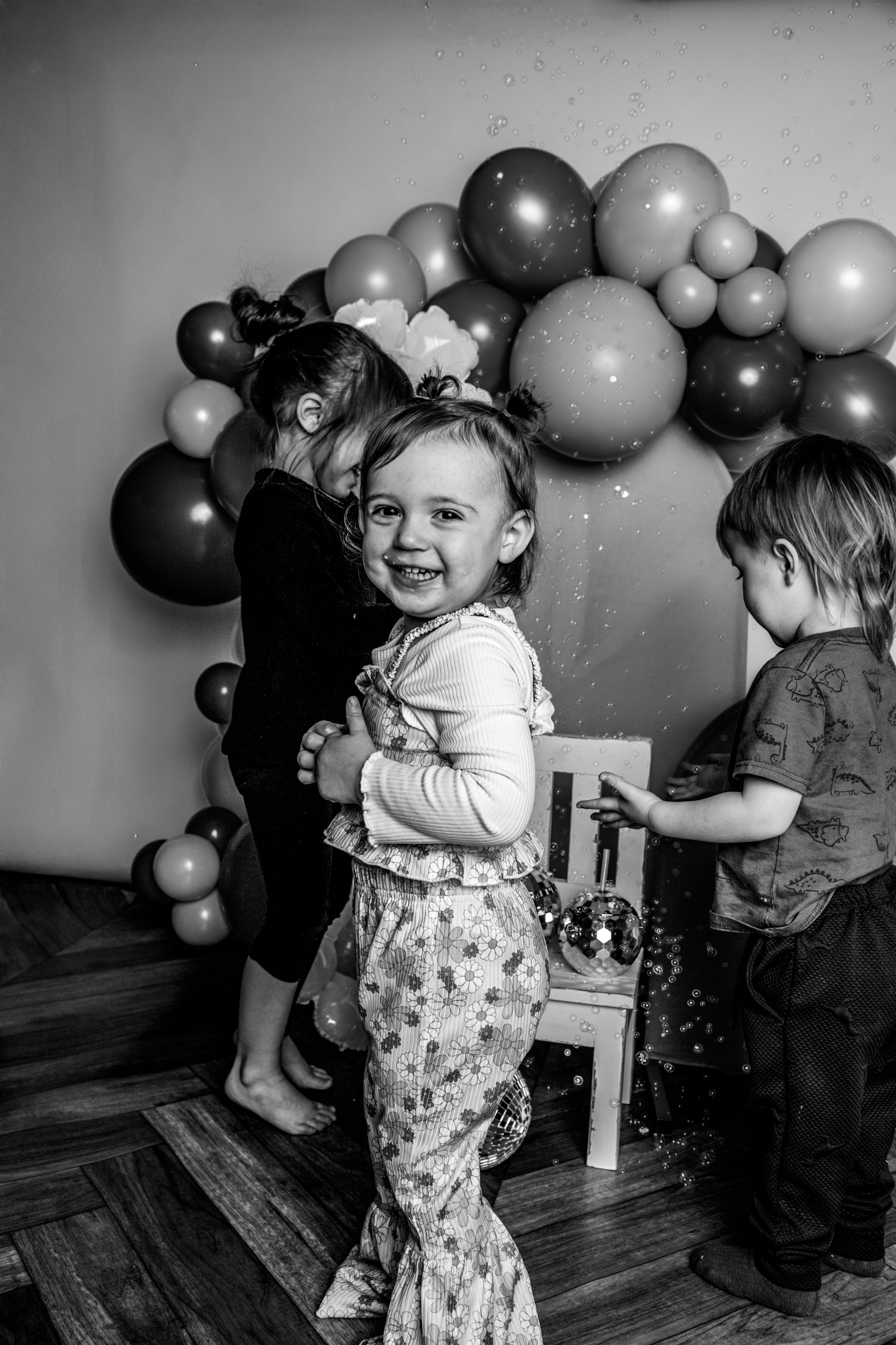 Children celebrating a birthday indoors, with balloons and a decorated background.