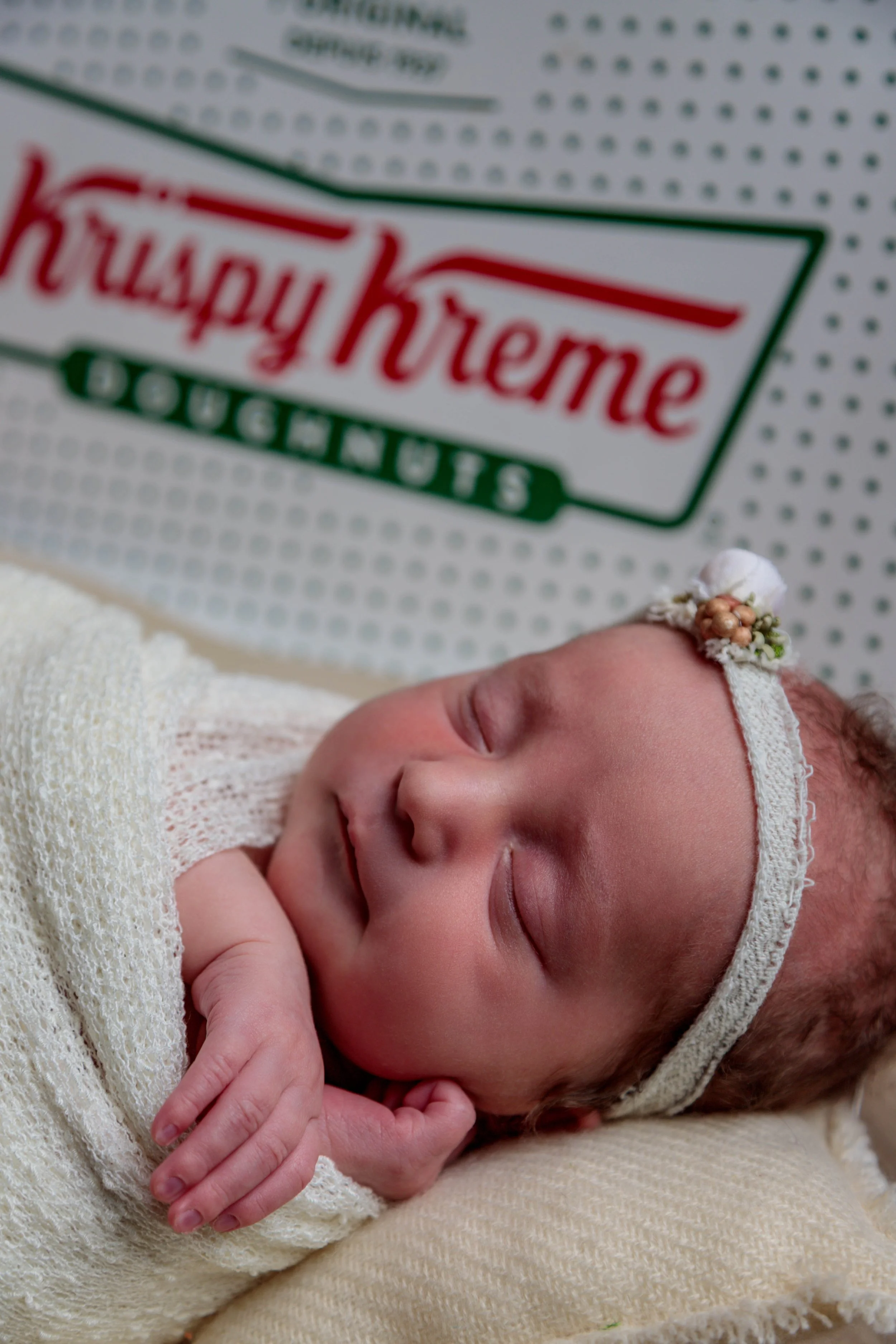 A newborn baby sleeping peacefully, wrapped in a white blanket, with a hospital band on their wrist, in front of a Health-Quest hospital logo.