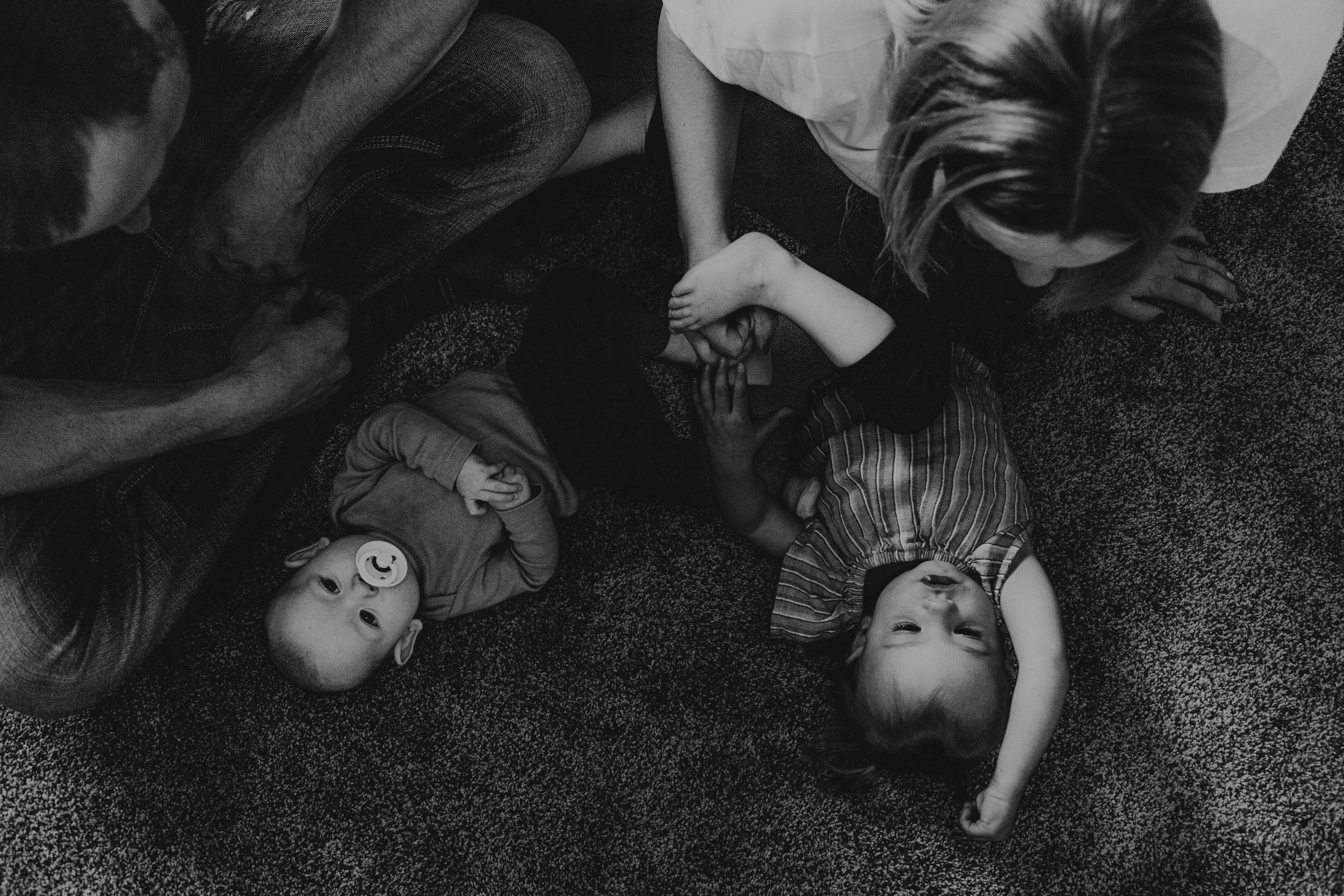 Eight children lying on a carpeted floor, some with pacifiers, viewed from above, in black and white.