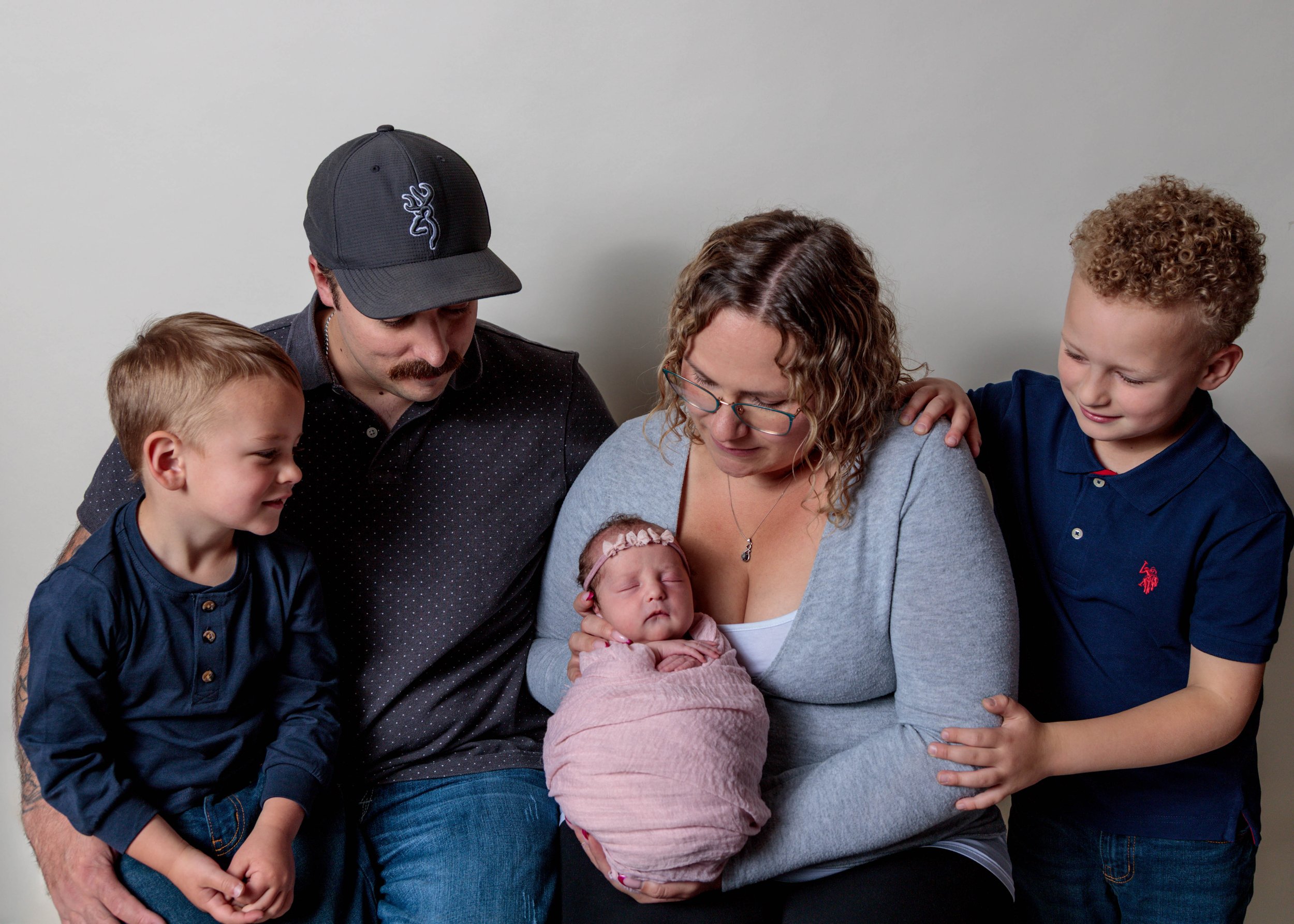 A family of six holding a newborn baby together, with a plain gray background.