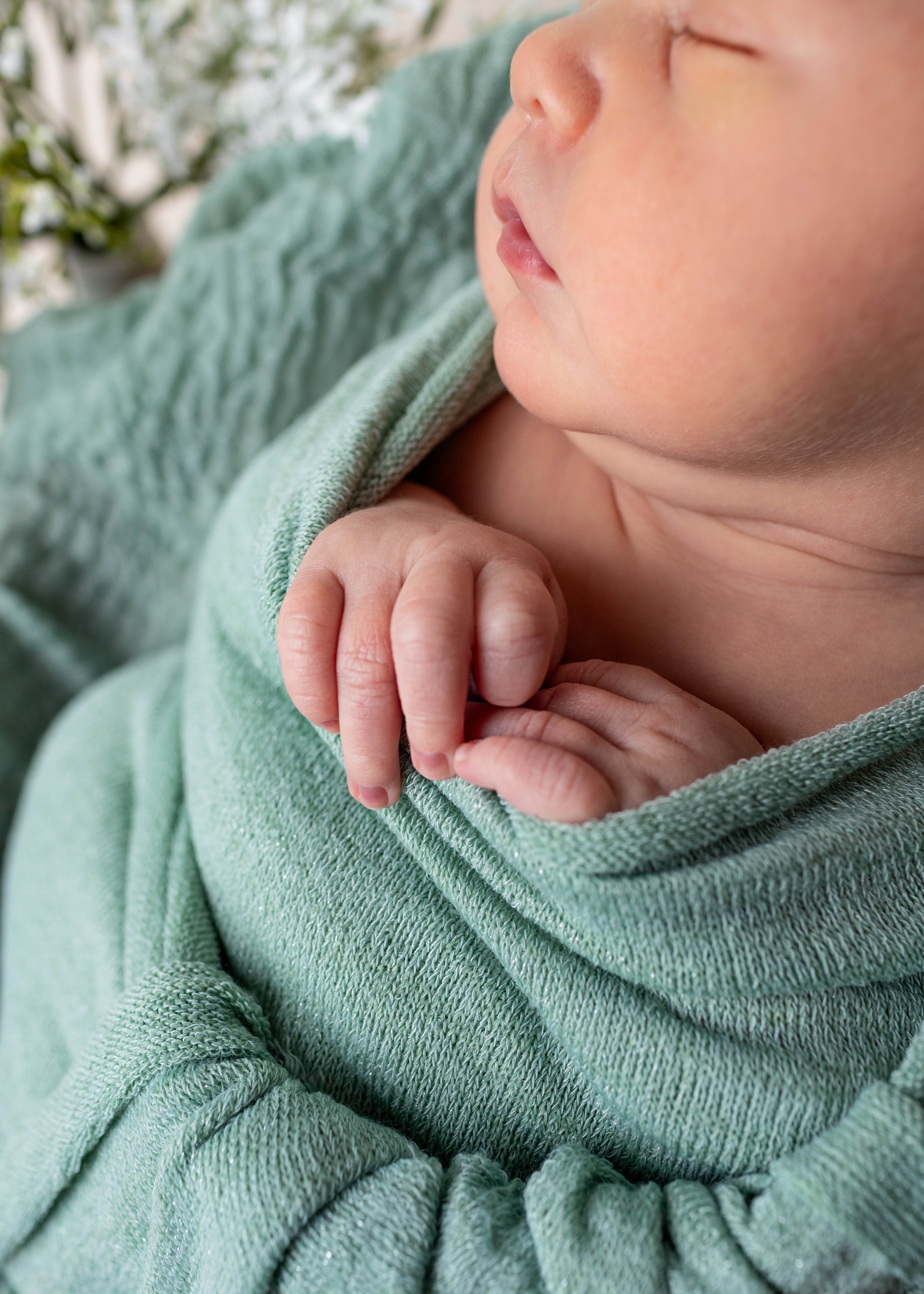 Close-up of a sleeping baby's face with hands clasped, wearing a green hoodie.
