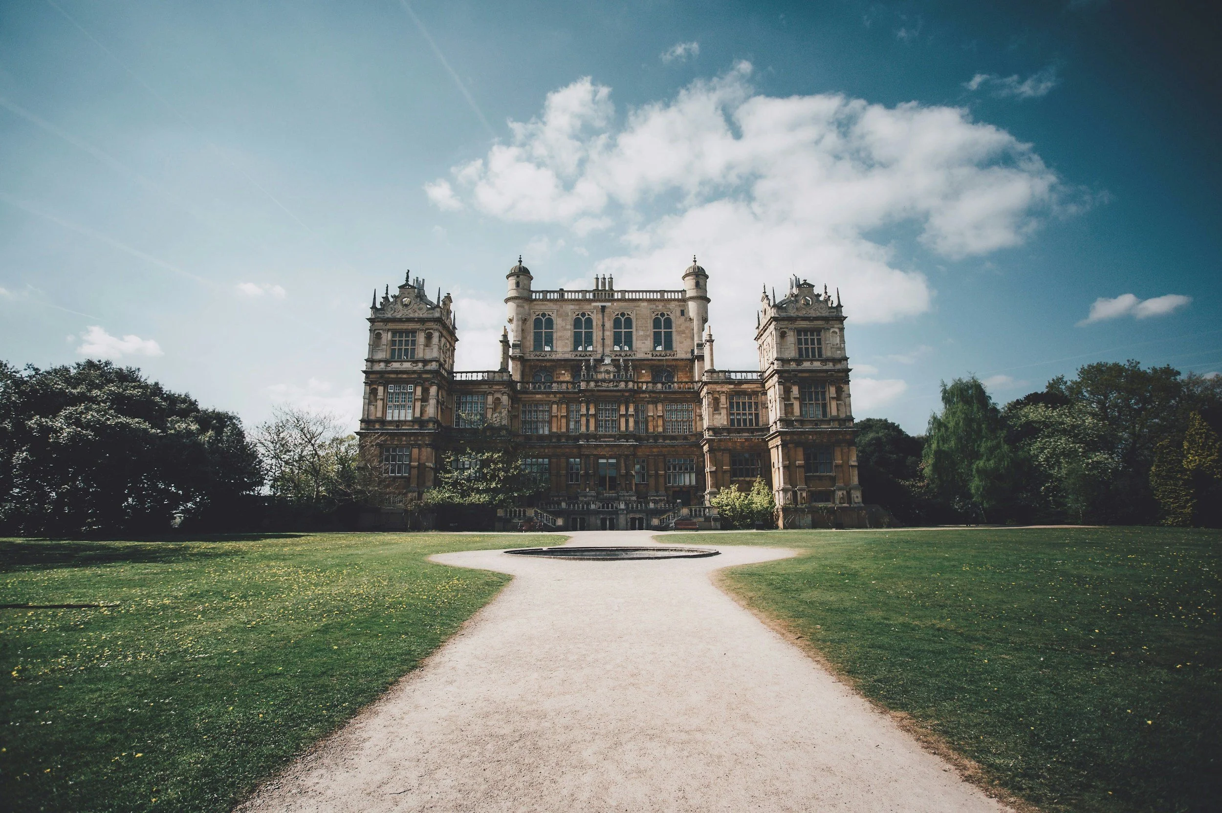 Historic manor house in Nottingham with ornate architecture surrounded by a large garden and trees under a blue sky with clouds.