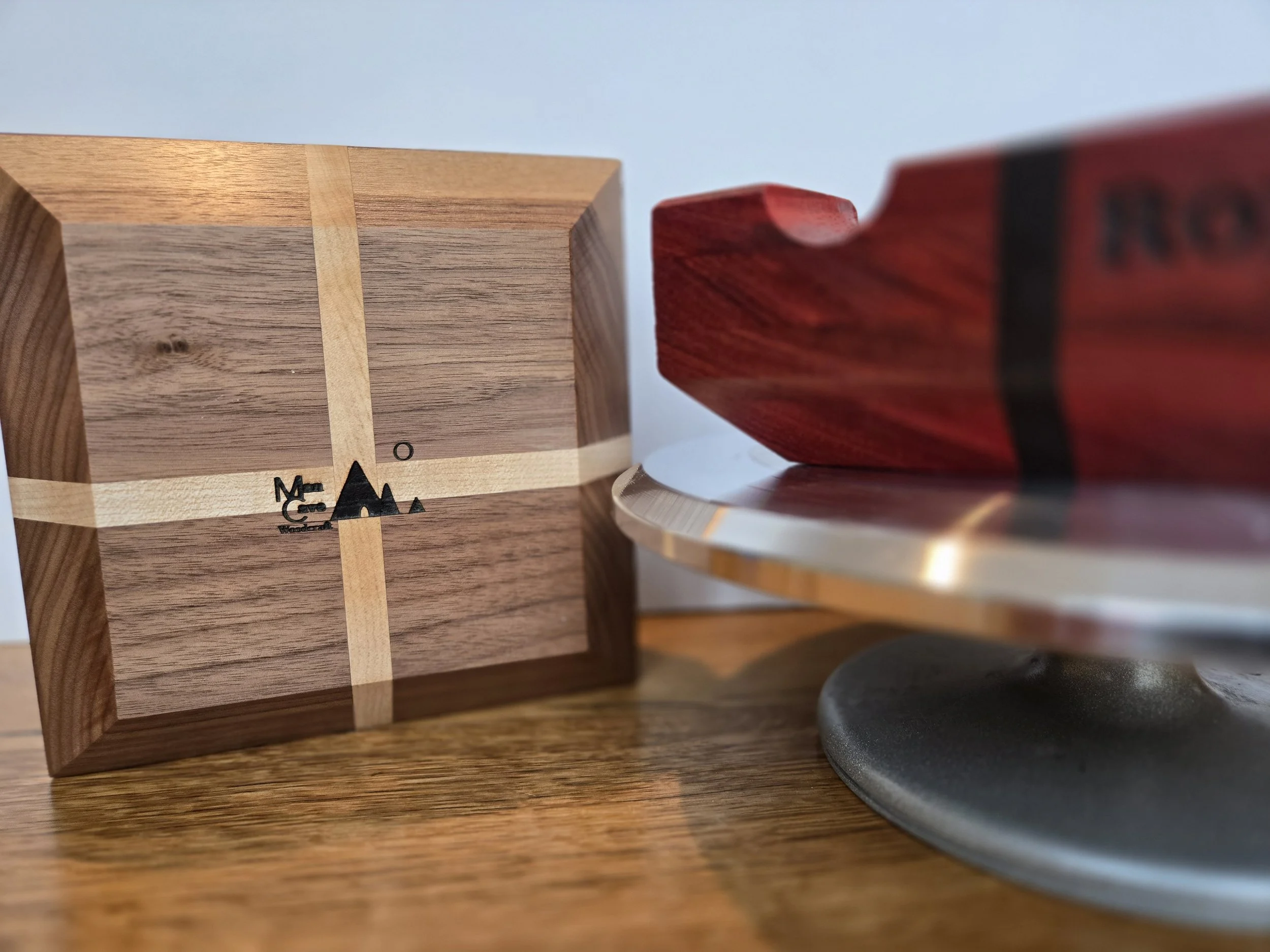 Close-up of a wooden clock with a minimalist design, showing the ashtrays with black markings and wooden background, next to a red wooden object, all on a wooden surface.