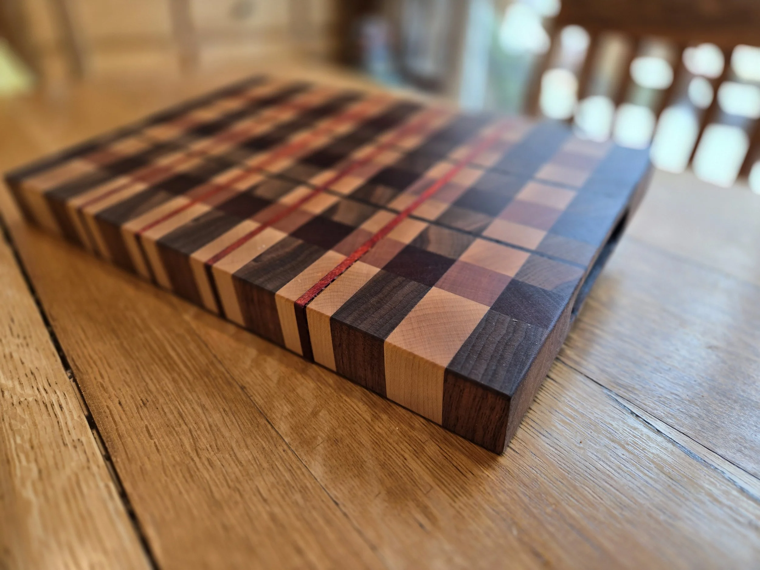 A wooden cutting board with a checkered pattern made of various wood pieces, placed on a wooden table.