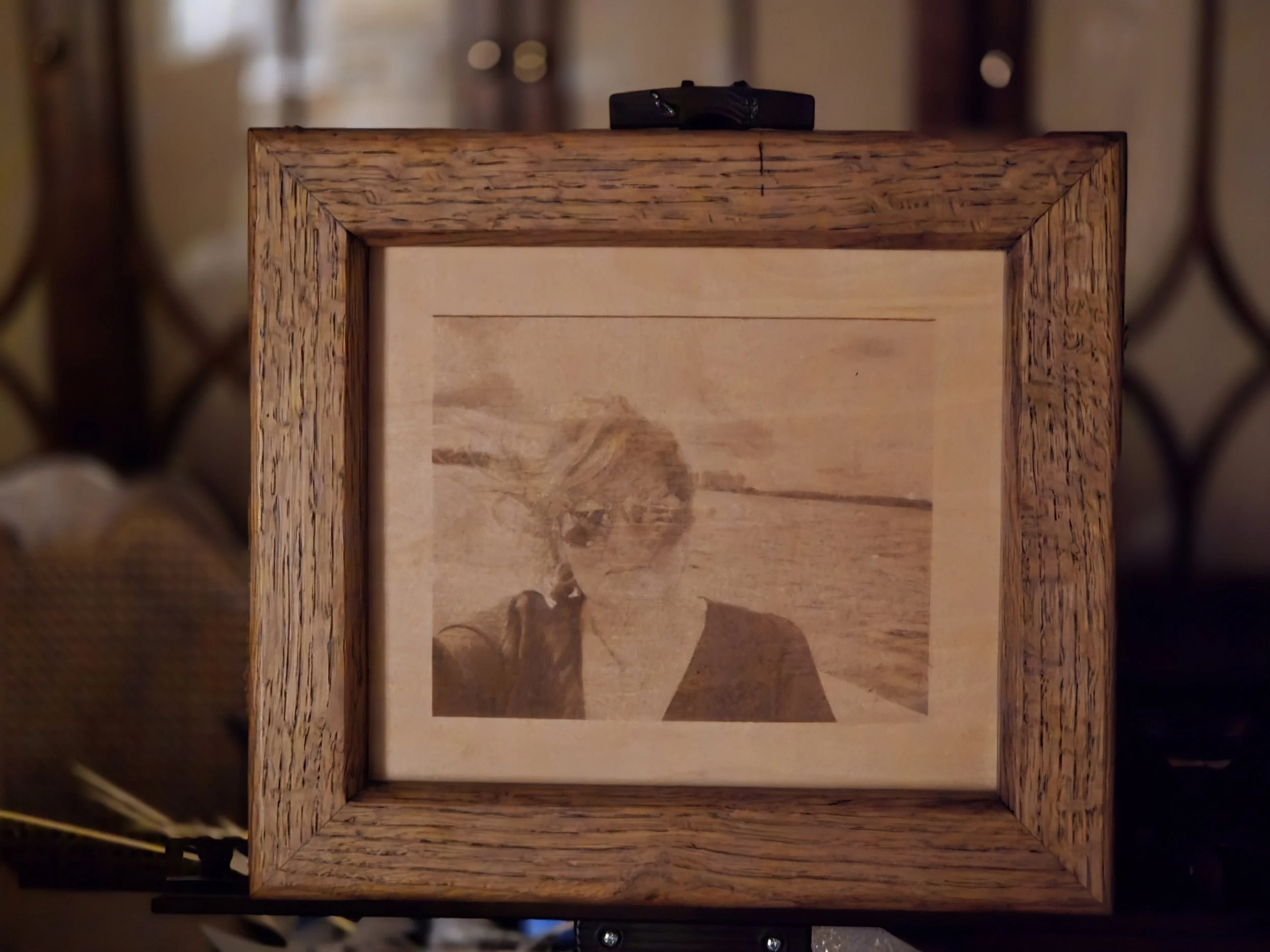 A wooden picture frame containing an old, faded sepia-toned photograph of a woman at the beach.