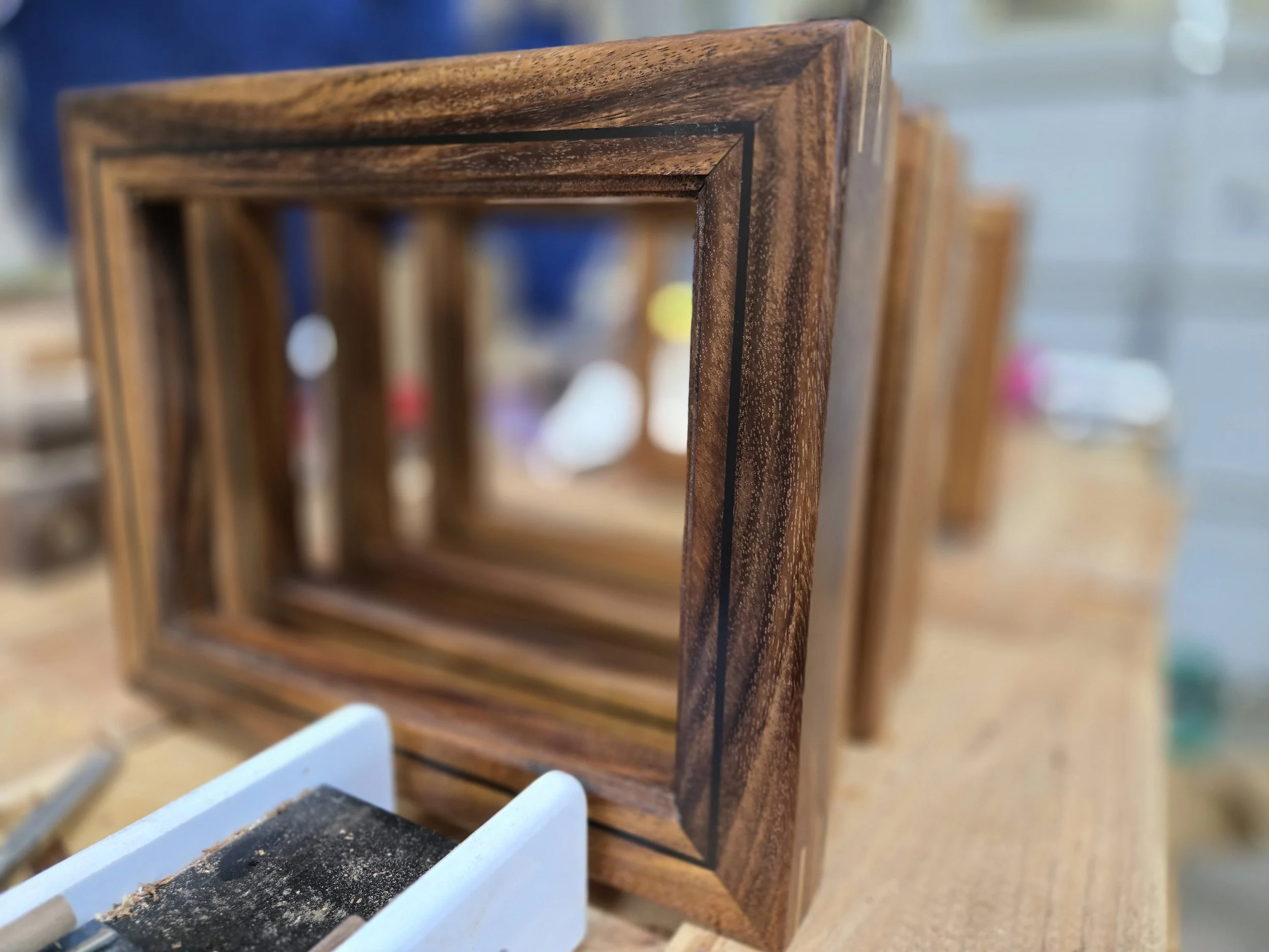 Set of wooden frames with black lines on the edges, placed on a wooden workbench in a woodworking shop.