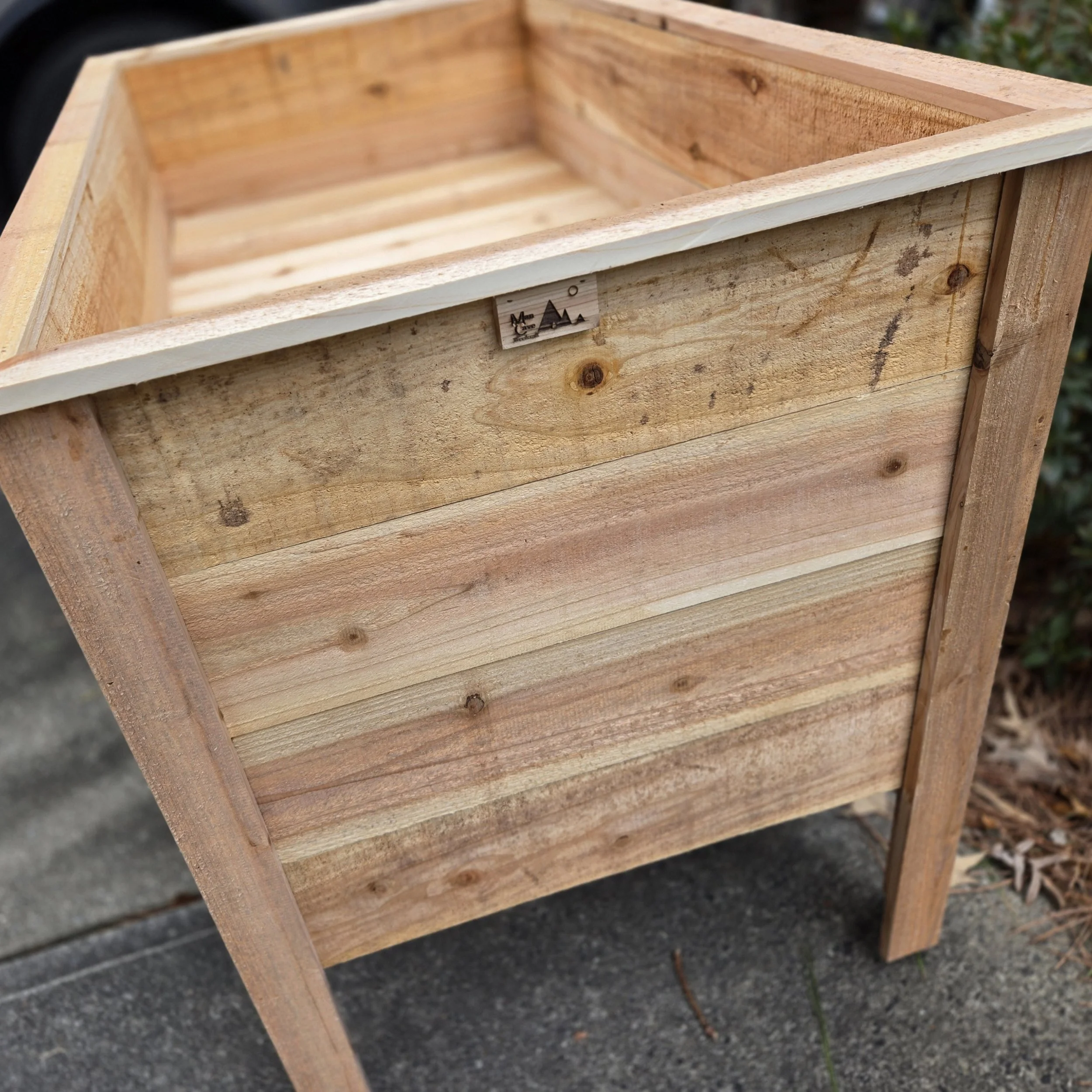 A wooden planter box with a rectangular shape, made of light-colored wood, placed outdoors on a concrete surface.