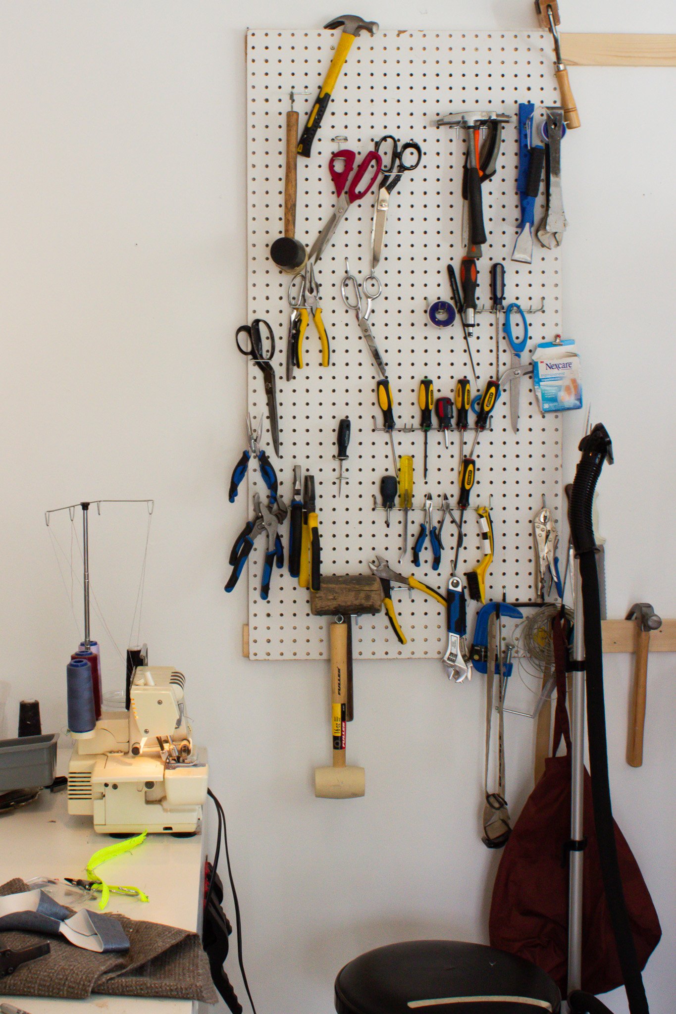 Pegboard with various tools hanging on it, including hammers, scissors, screwdrivers, pliers, and a saw, in a workshop setting.