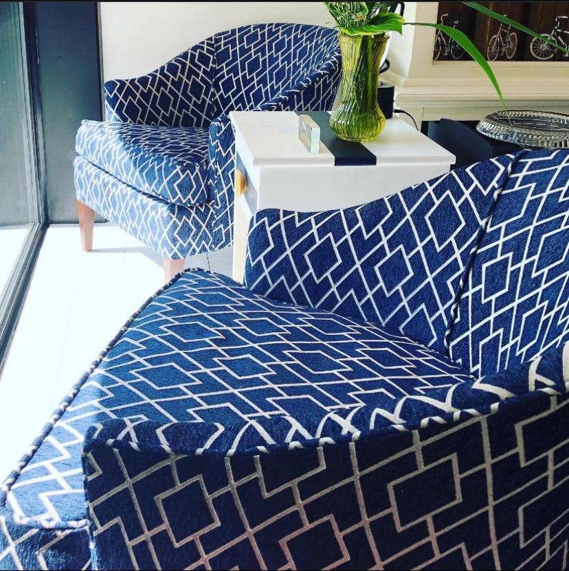 Living room with two blue patterned armchairs, a white side table with a green plant in a vase, and a piano in the background.