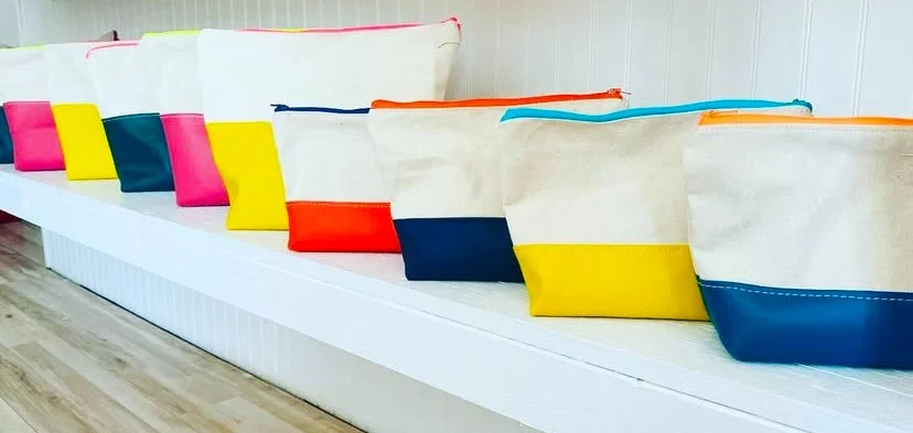 Multiple colorful tote bags lined up on a white shelf against a white wall.